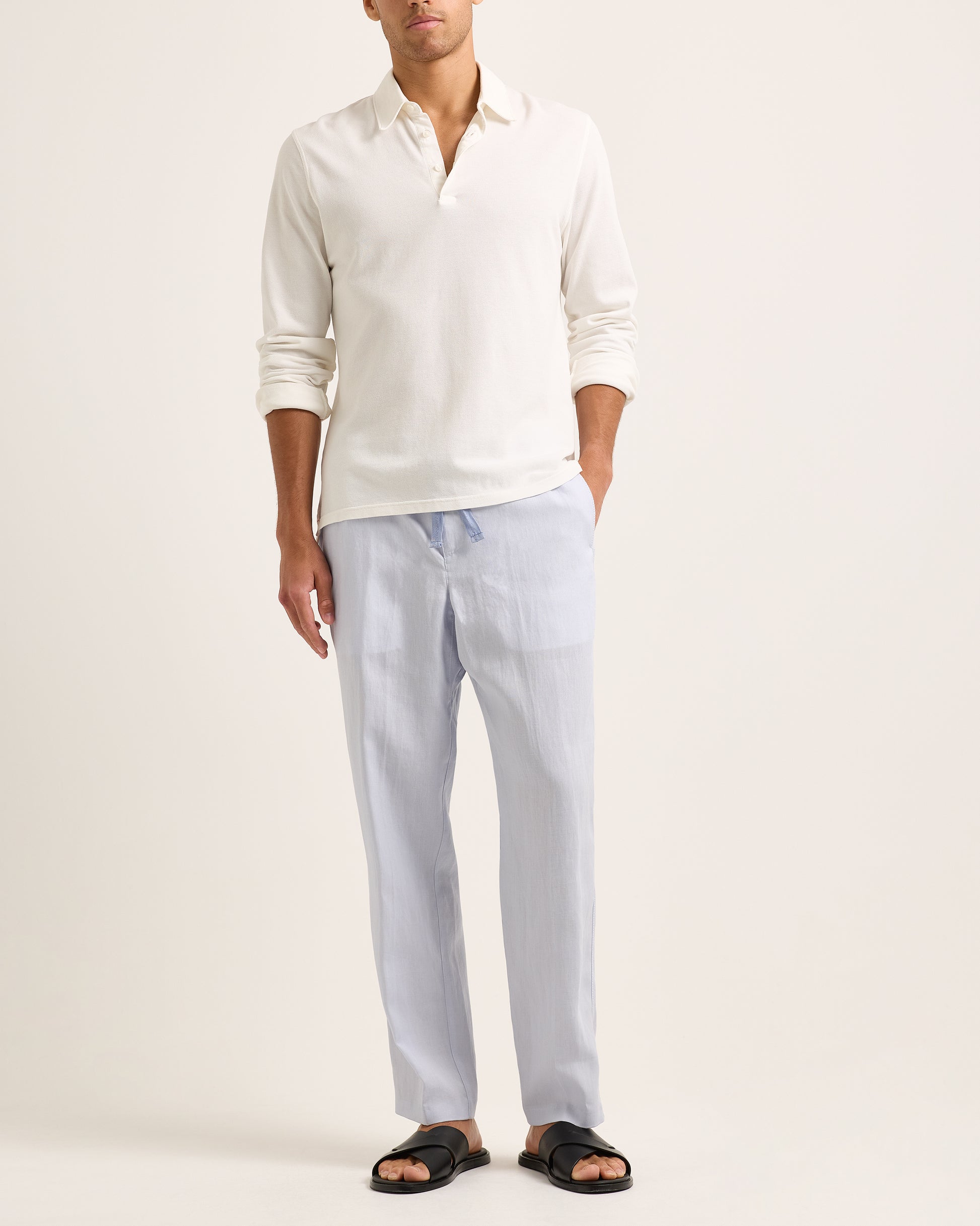Model wearing white long-sleeve polo shirt with blue trousers on a white background