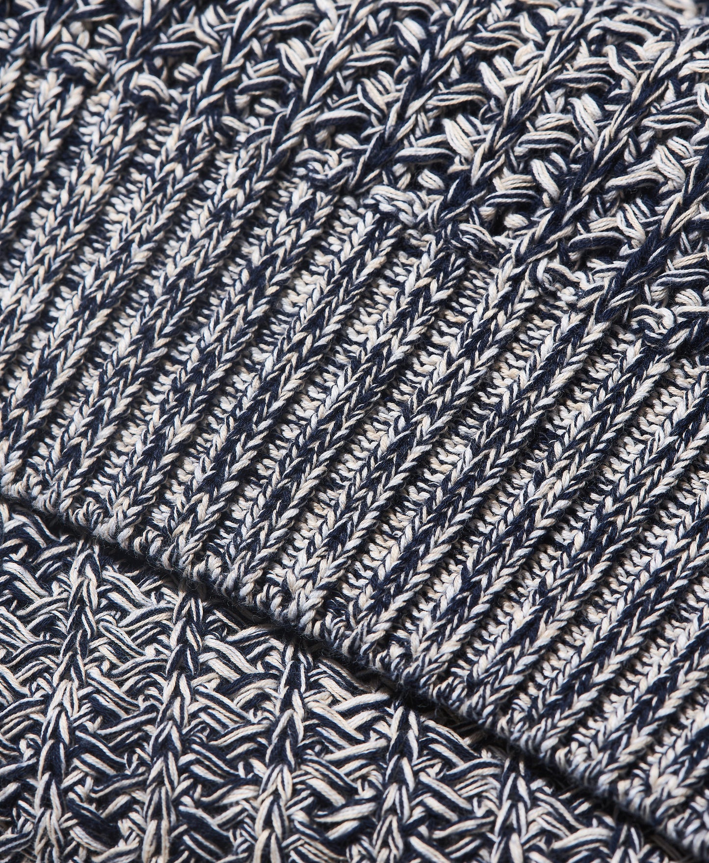 Close-up of a marled knit fabric with a ribbed cuff, showing a textured pattern of navy blue, white, and gray yarn.