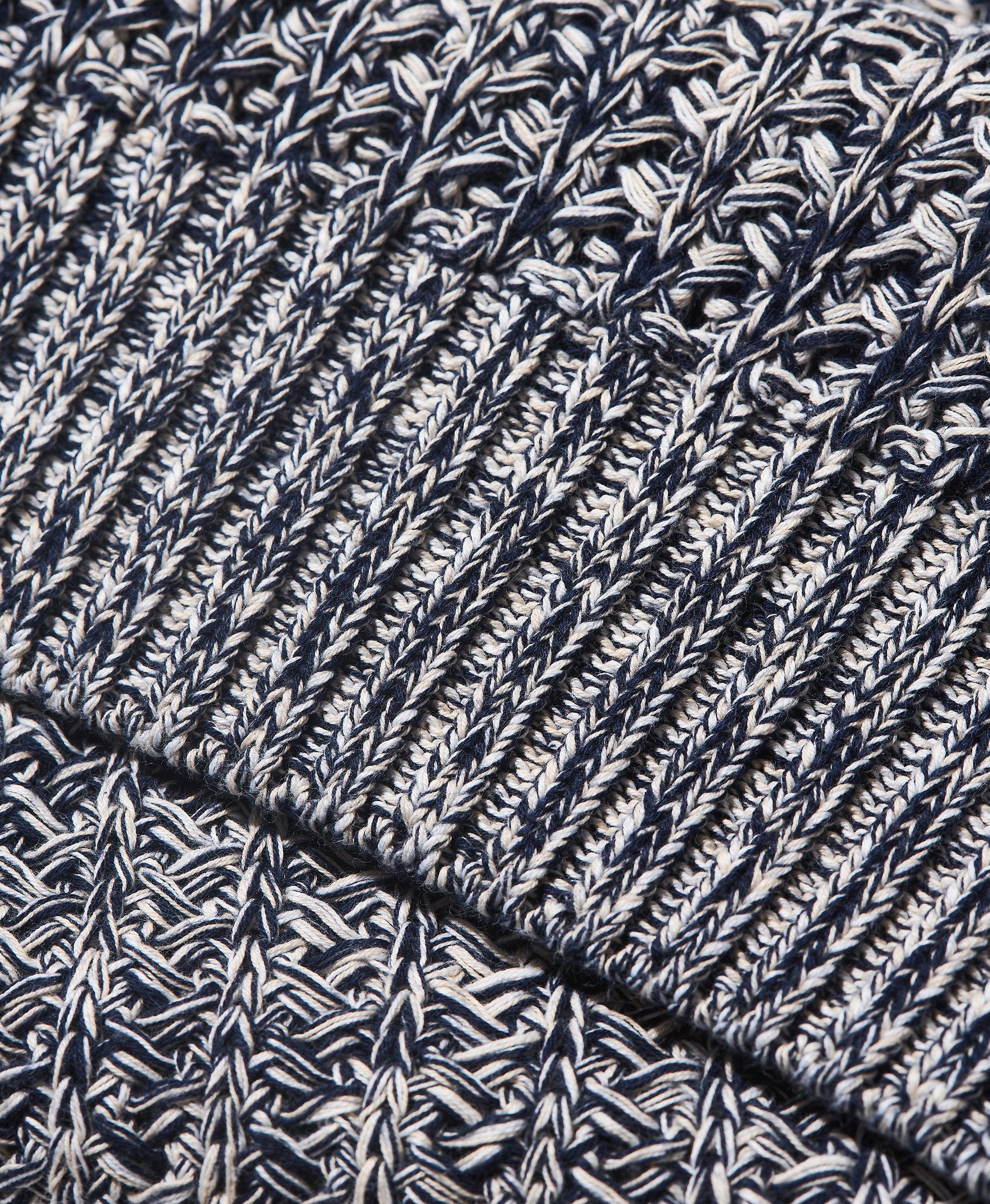 Close-up of a marled knit fabric with a ribbed cuff, showing a textured pattern of navy blue, white, and gray yarn.