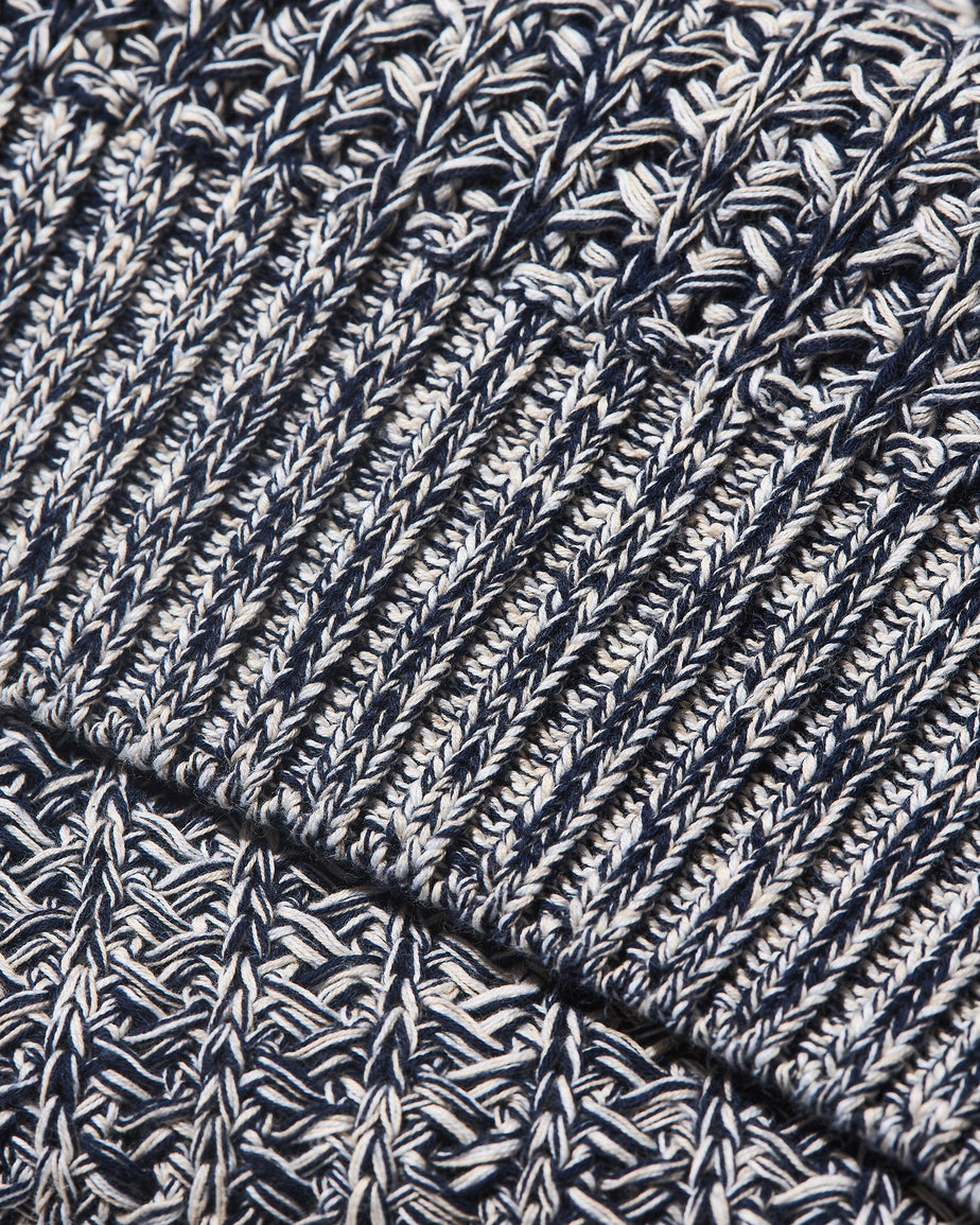Close-up of a navy and off-white heathered knit fabric with ribbed and textured stitch patterns.