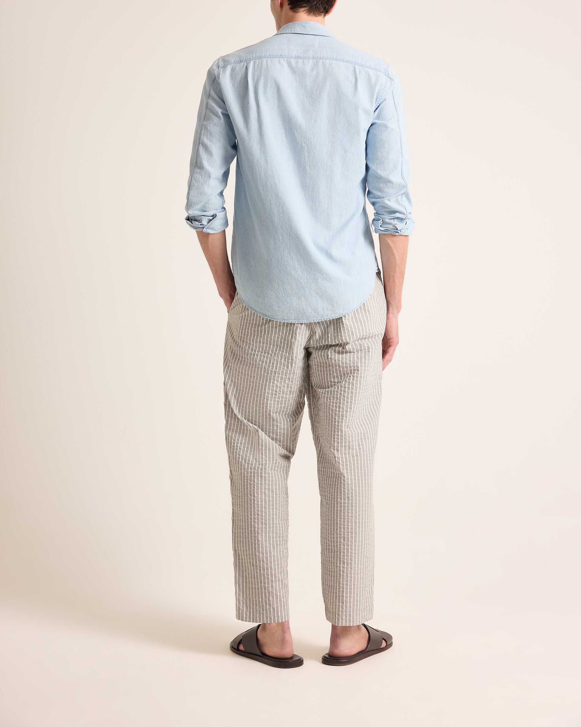 Person wearing a light blue shirt and plaid pants on a beige background