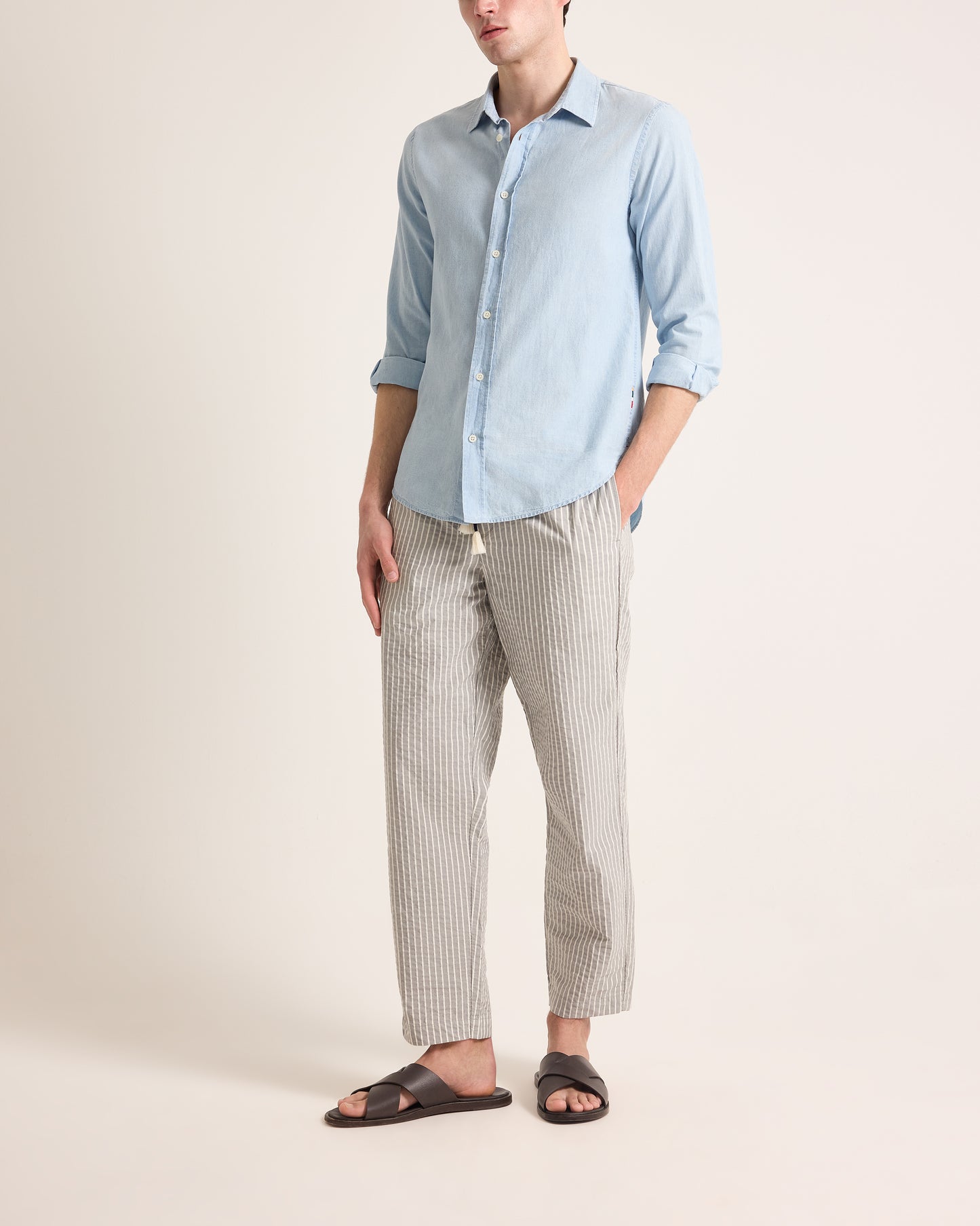 Person wearing a light blue button-up shirt and striped pants on a beige background