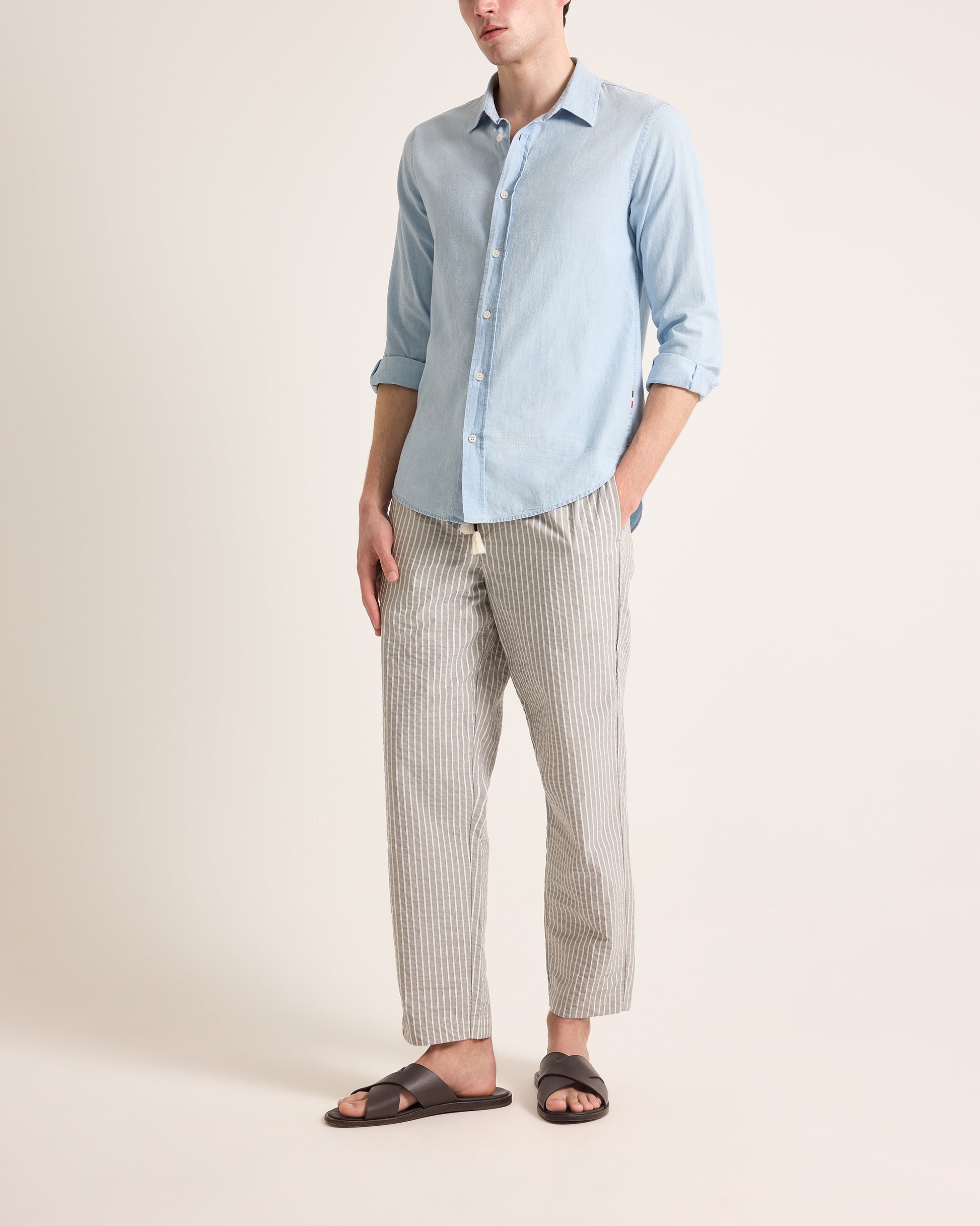 Person wearing a light blue button-up shirt and striped pants on a beige background