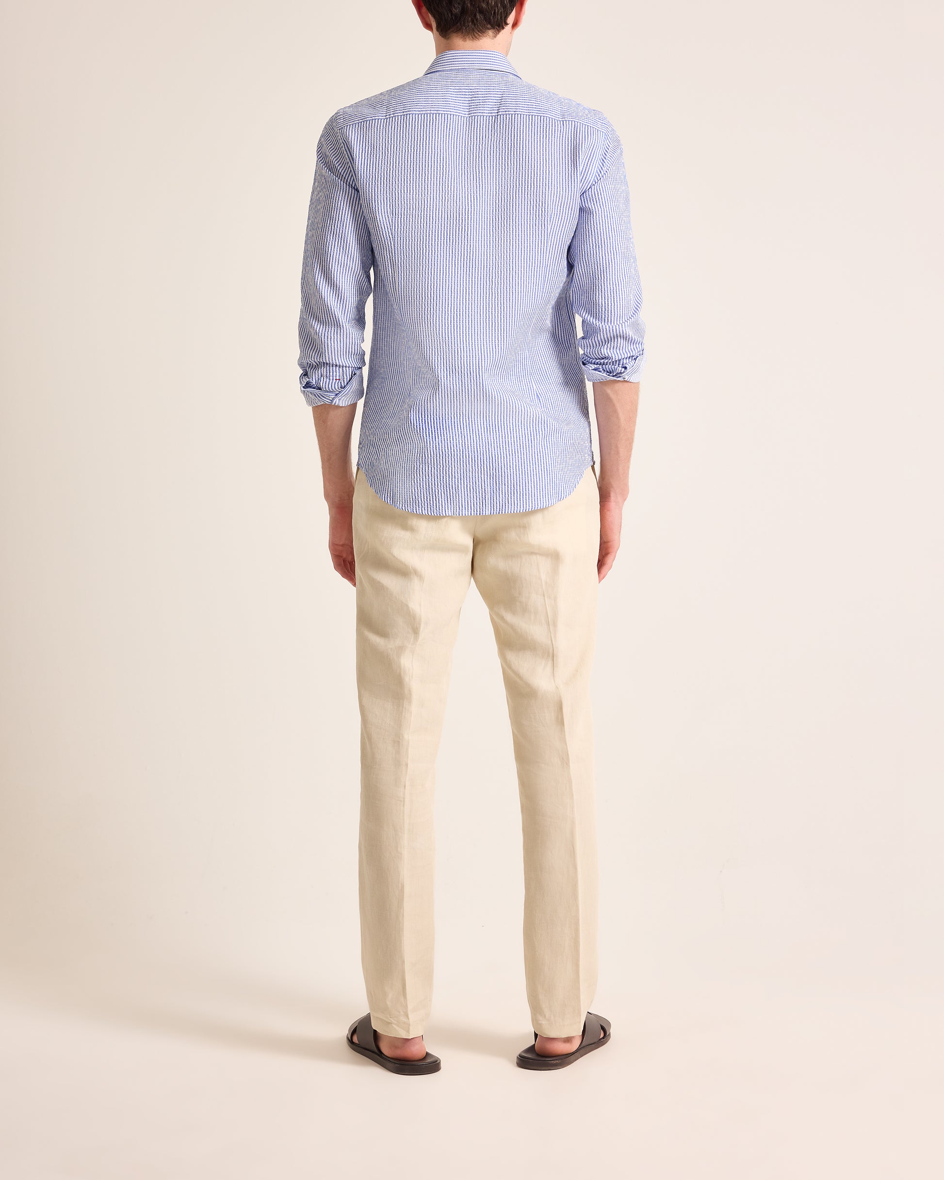 Person wearing a light blue striped shirt and beige pants on a plain background