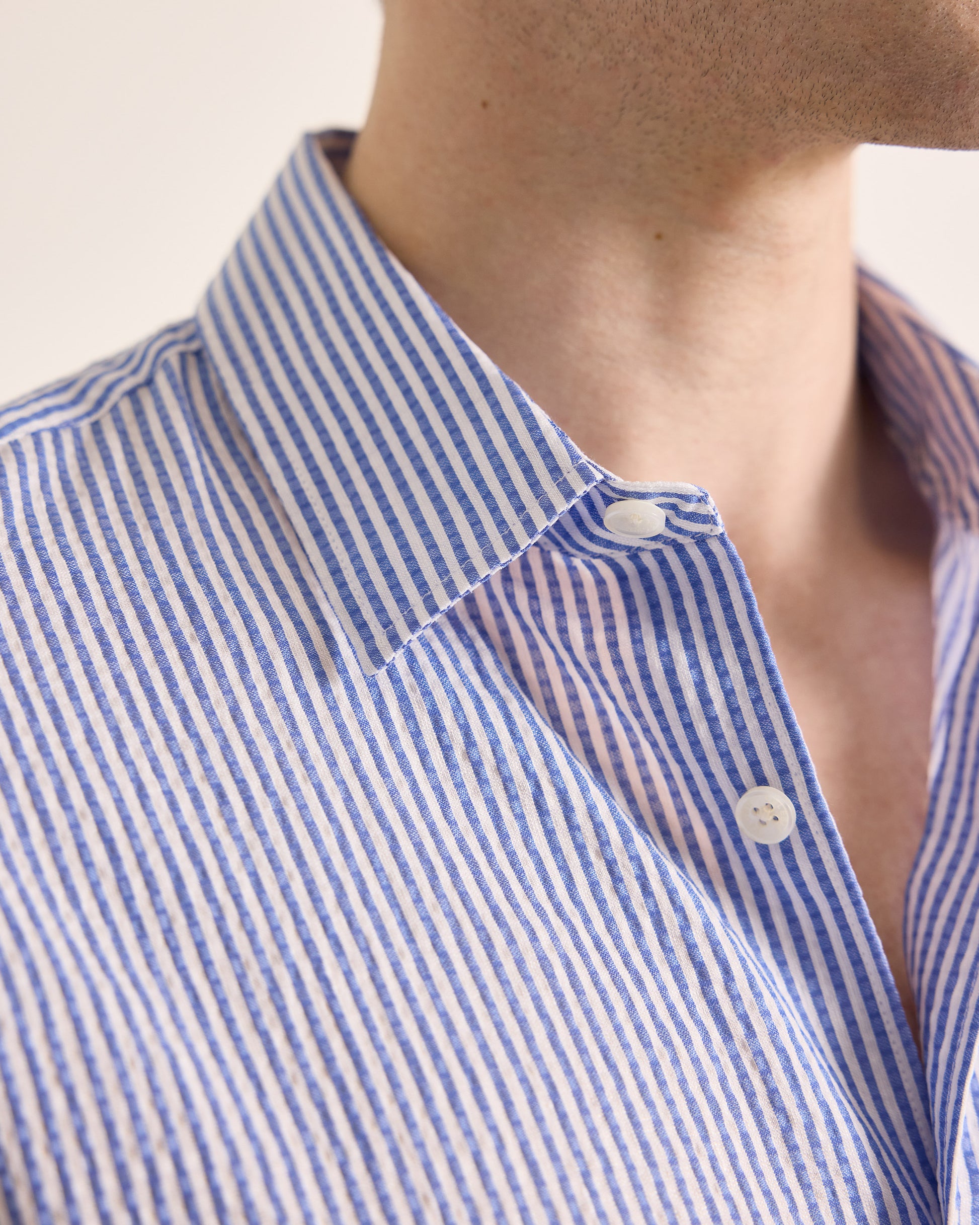 Close-up of a person wearing a blue and white striped shirt with a neutral background