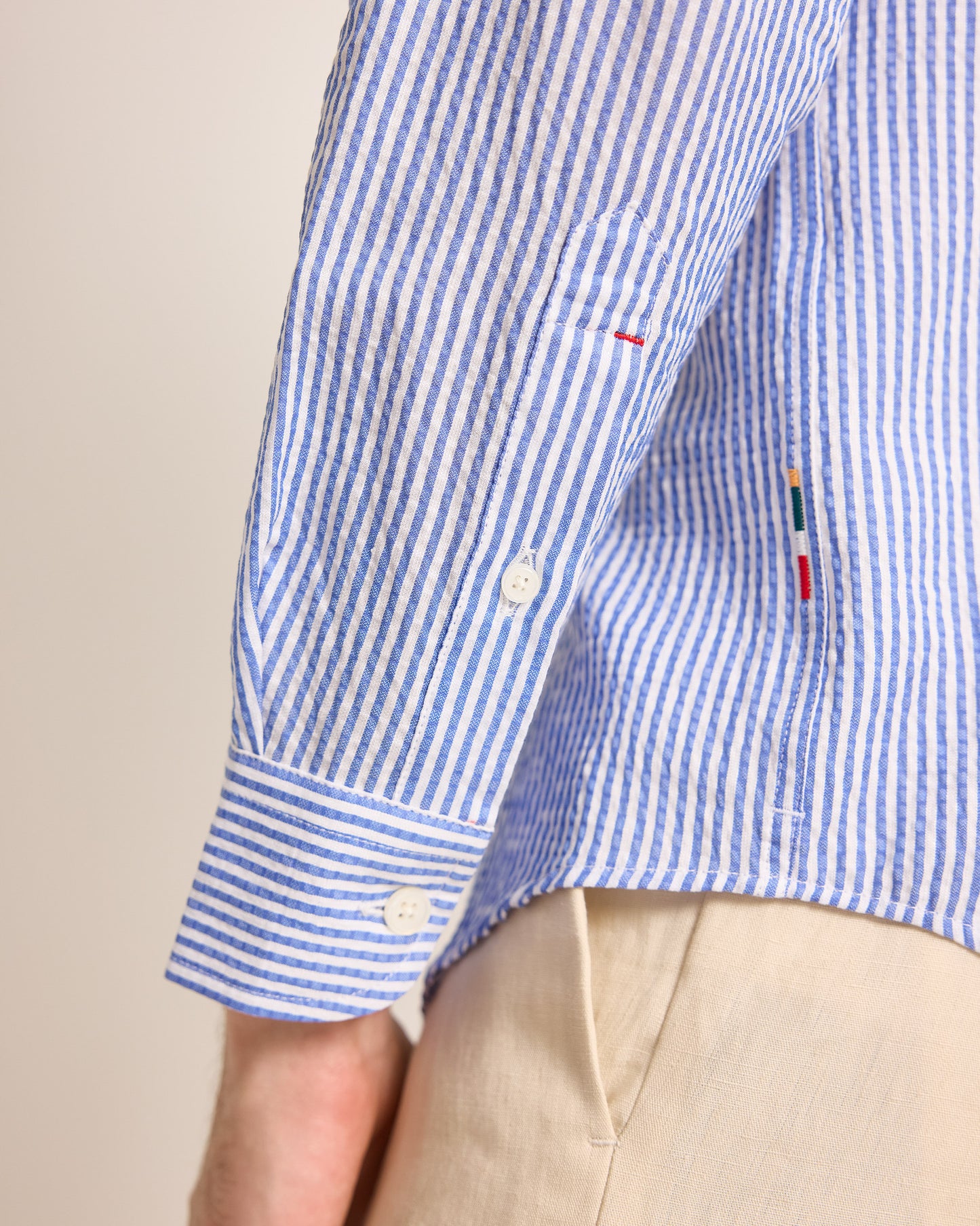 Close-up of a blue and white striped shirt with a brand logo on a beige background