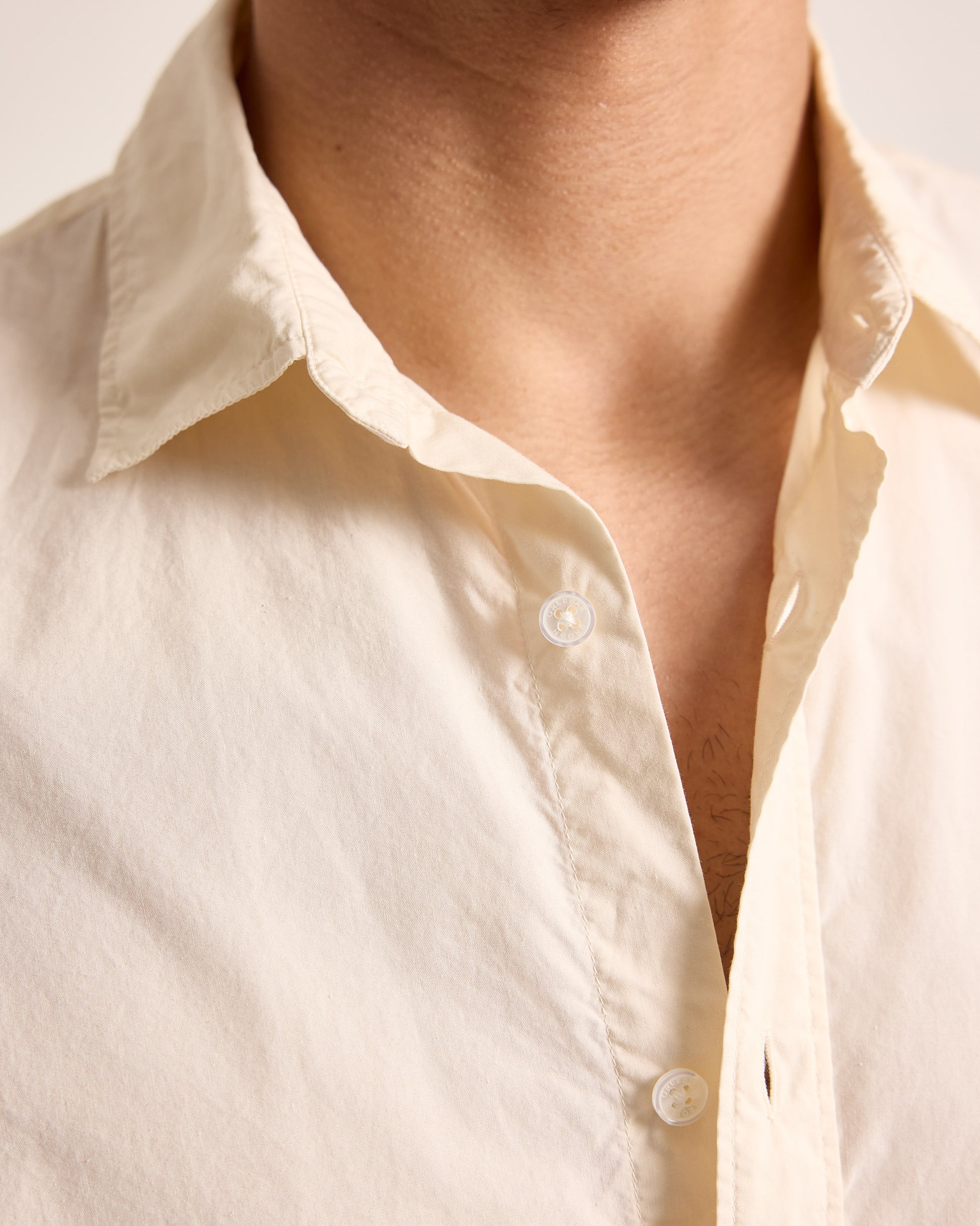 Close-up of a person wearing a light-colored shirt with a neutral background
