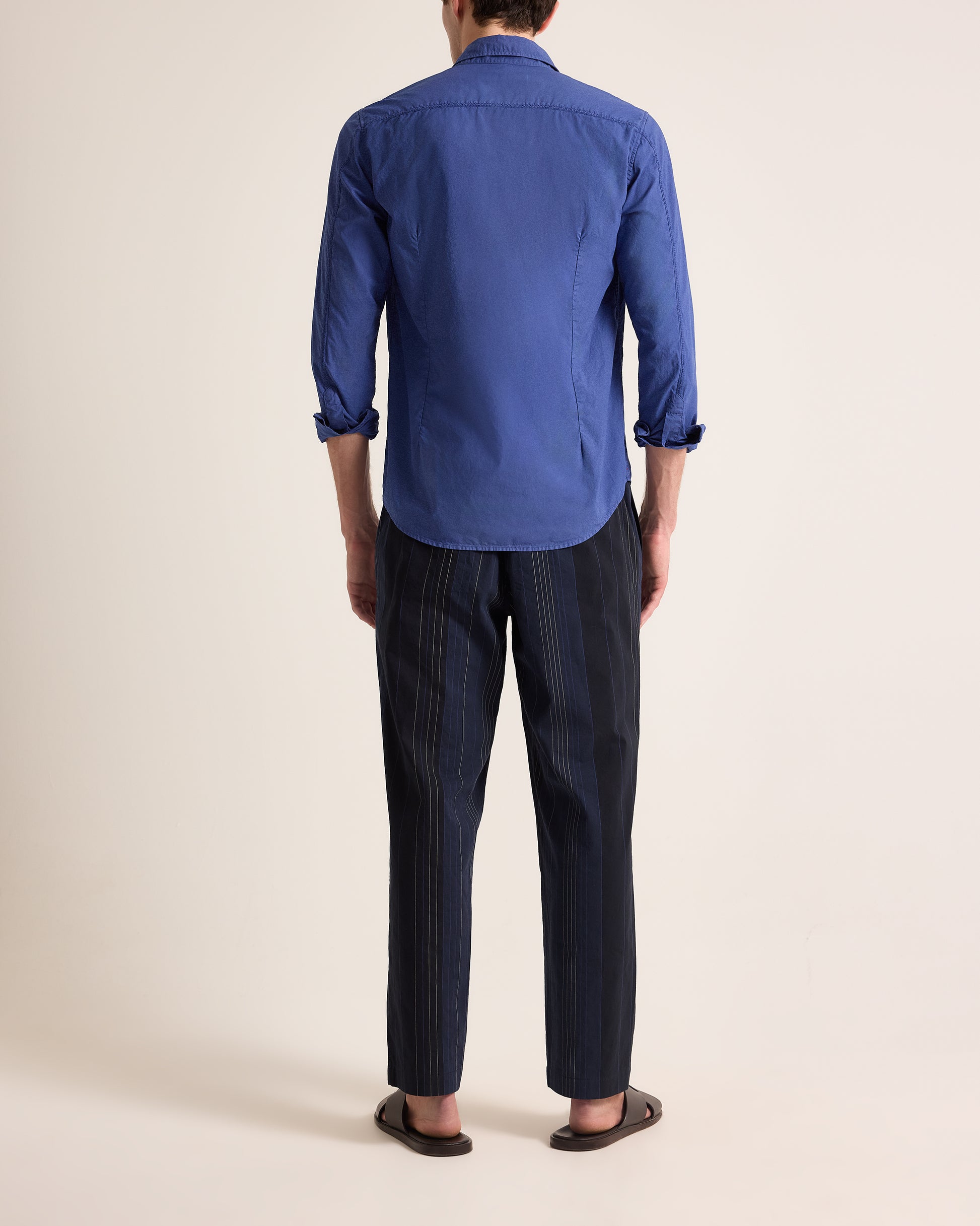 Person wearing a blue shirt and dark pants on a beige background