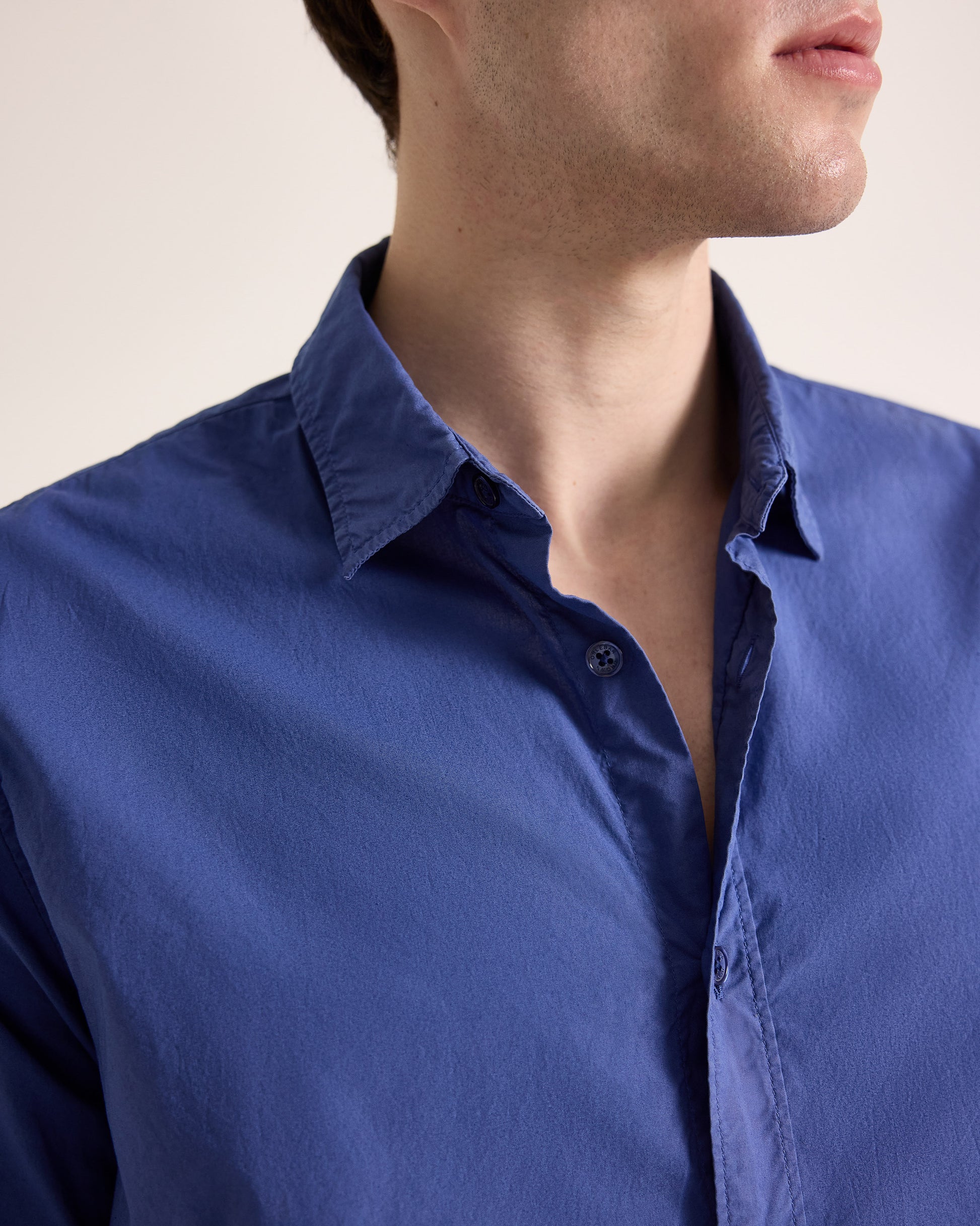 Close-up of a person wearing a blue shirt with a neutral background