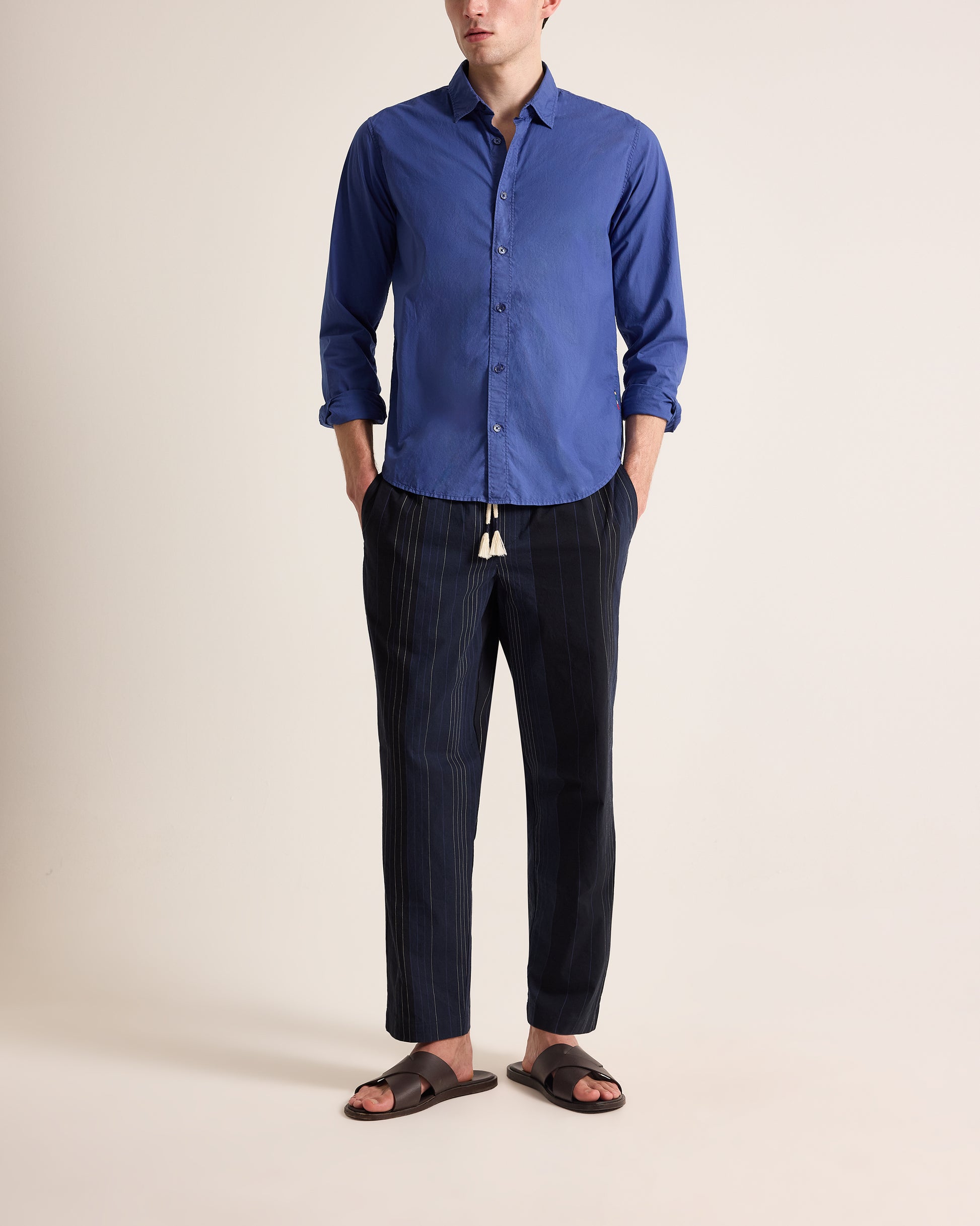 Person wearing a blue shirt and dark pants on a beige background