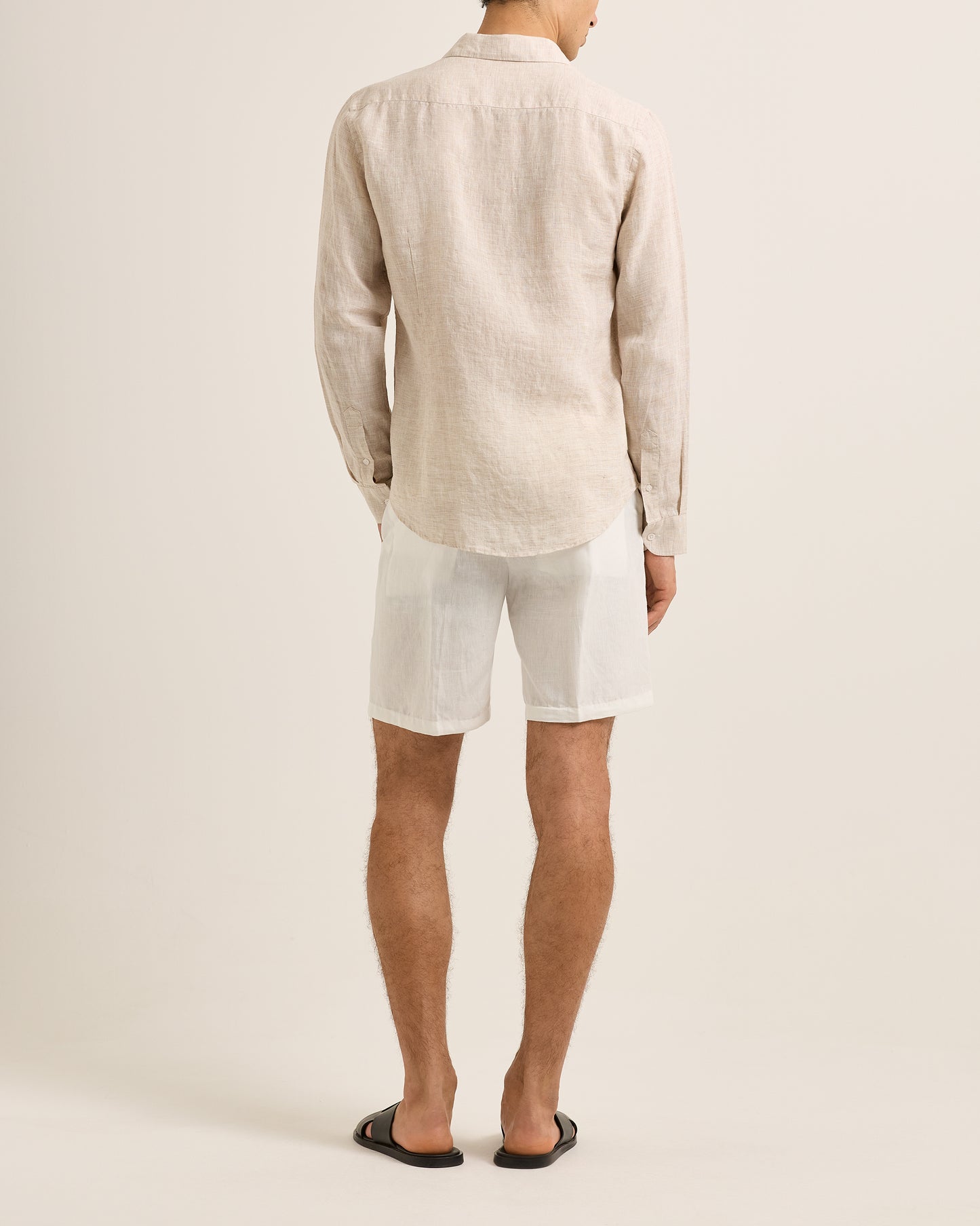 Person wearing a beige linen shirt and white shorts on a plain background