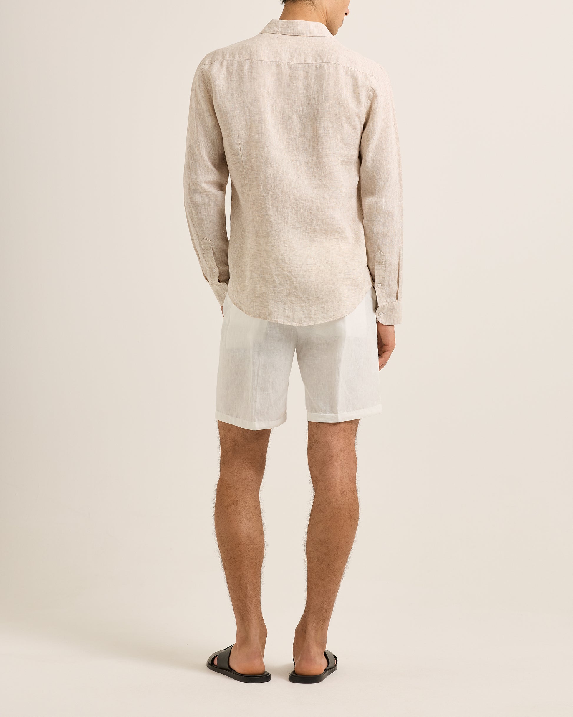 Person wearing a beige linen shirt and white shorts on a plain background
