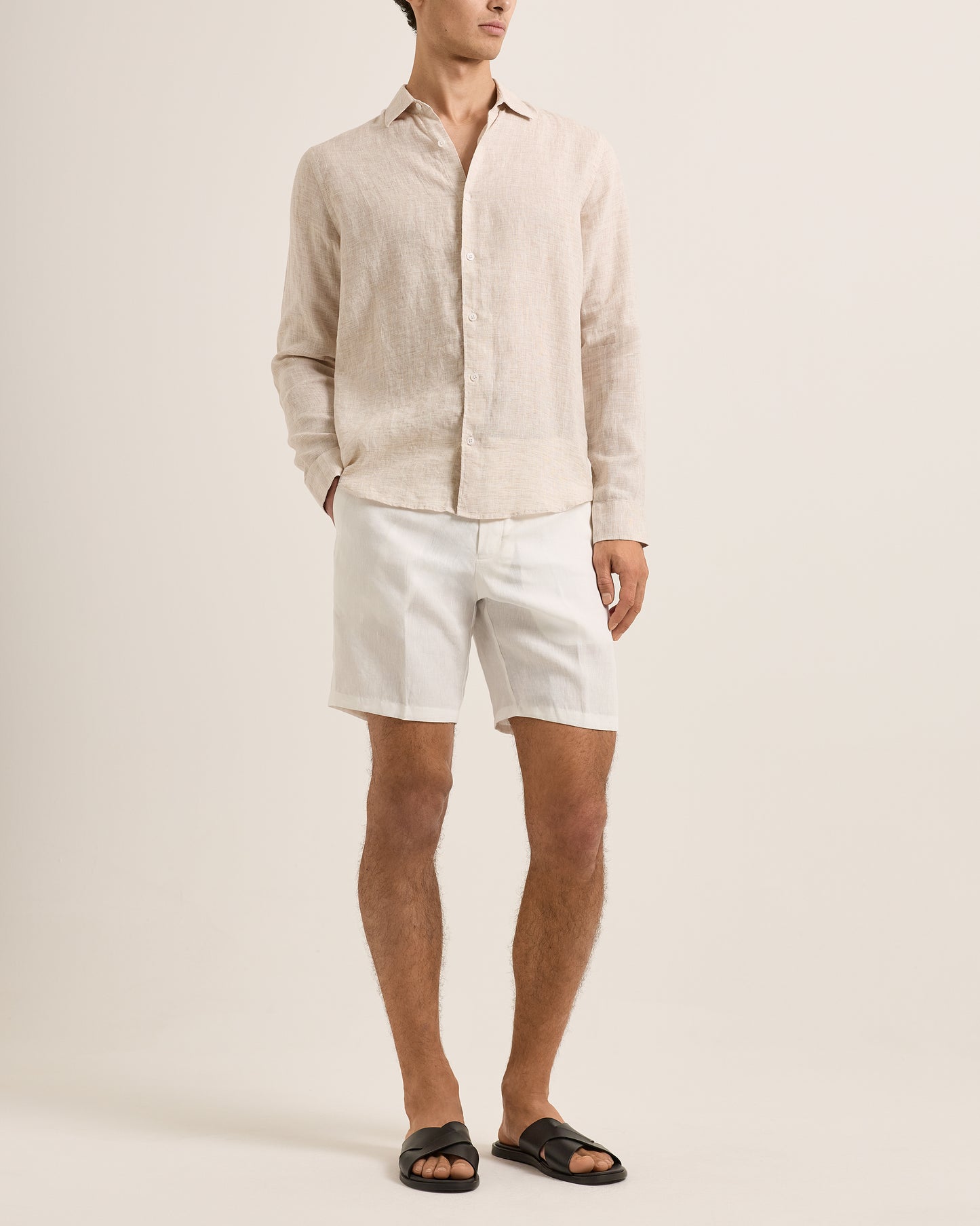 Person wearing a beige linen shirt and white shorts on a plain background