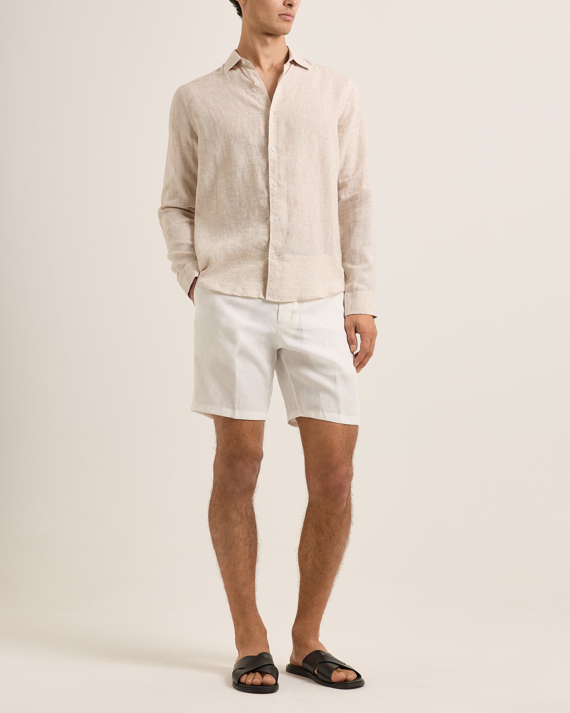 Person wearing a beige linen shirt and white shorts on a plain background