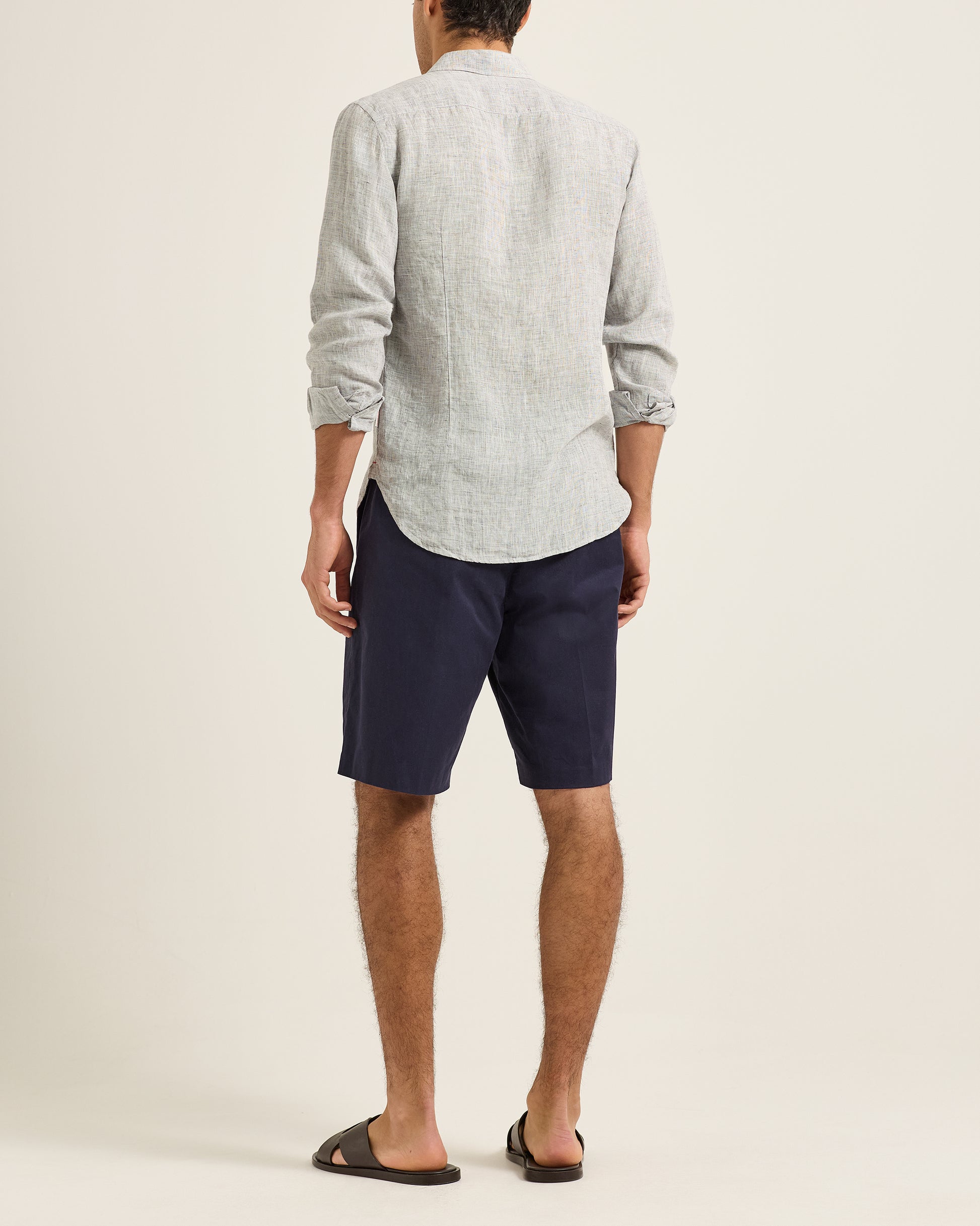 Man wearing a light gray shirt and navy shorts on a plain background