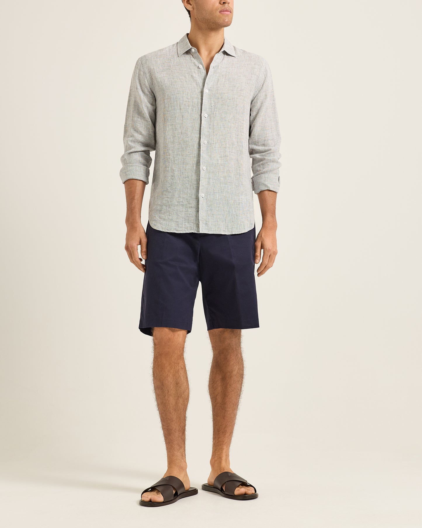 Man wearing a light gray button-up shirt and navy shorts on a beige background