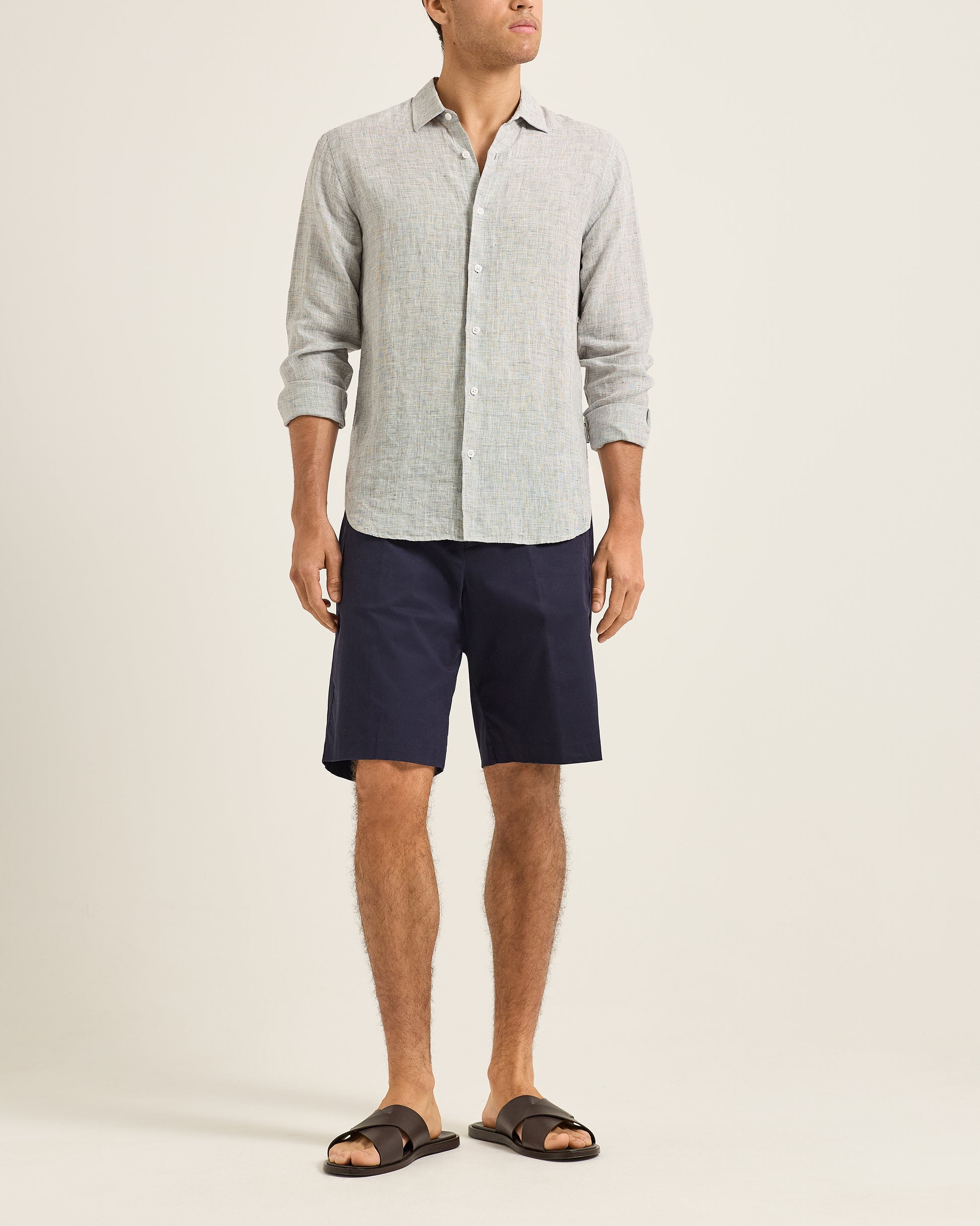 Man wearing a light gray button-up shirt and navy shorts on a beige background