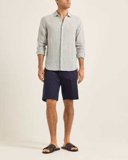 Man wearing a light gray button-up shirt and navy shorts on a beige background