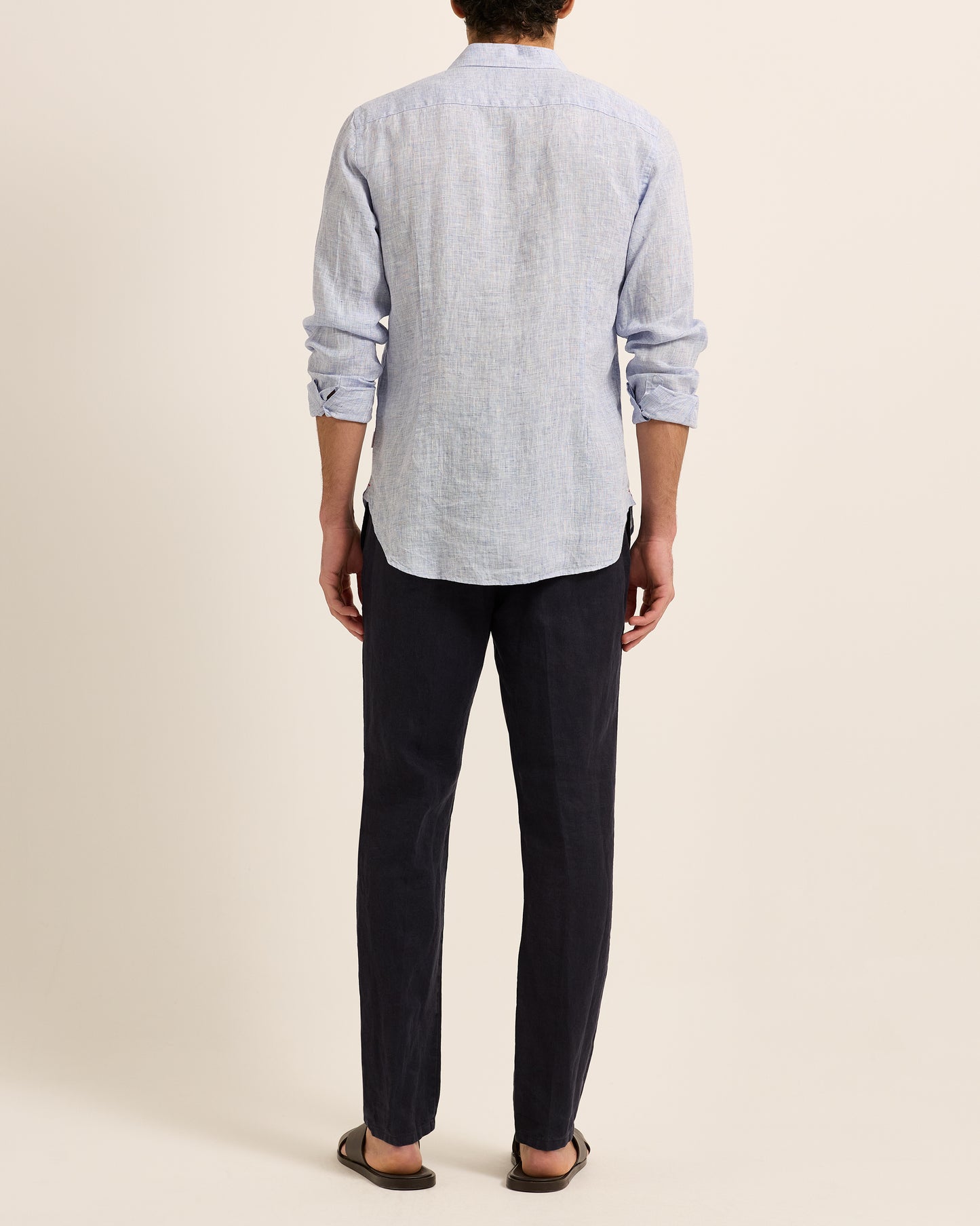 Man wearing light blue linen shirt with dark navy trousers on a white background