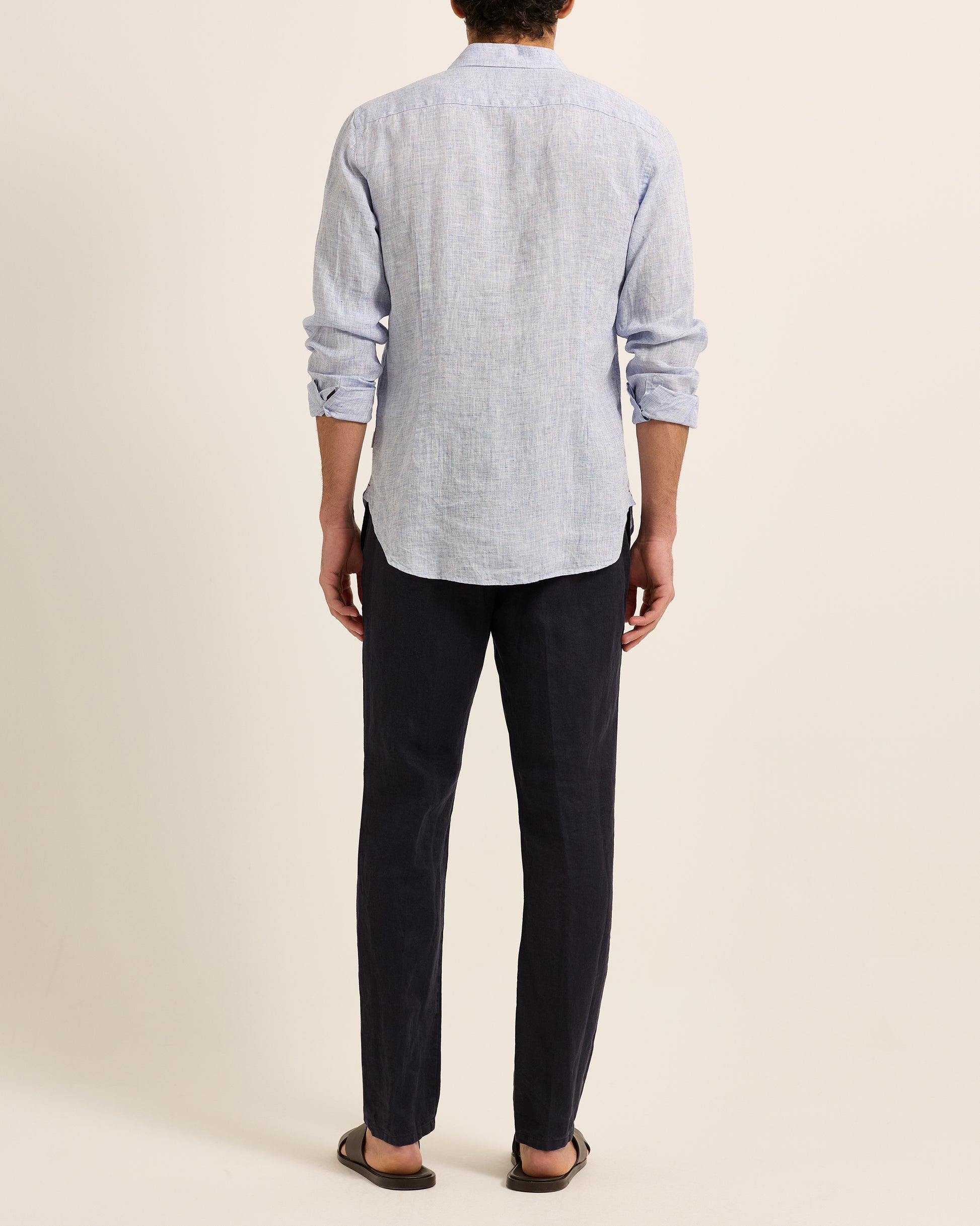 Man wearing light blue linen shirt with dark navy trousers on a white background