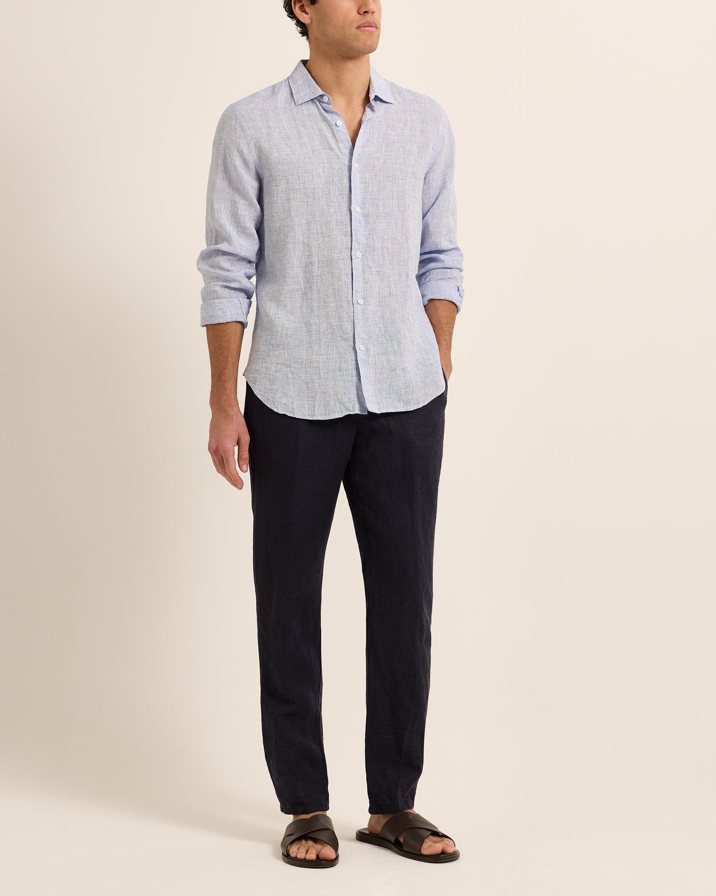 Man wearing light blue linen shirt with dark navy trousers on a white background