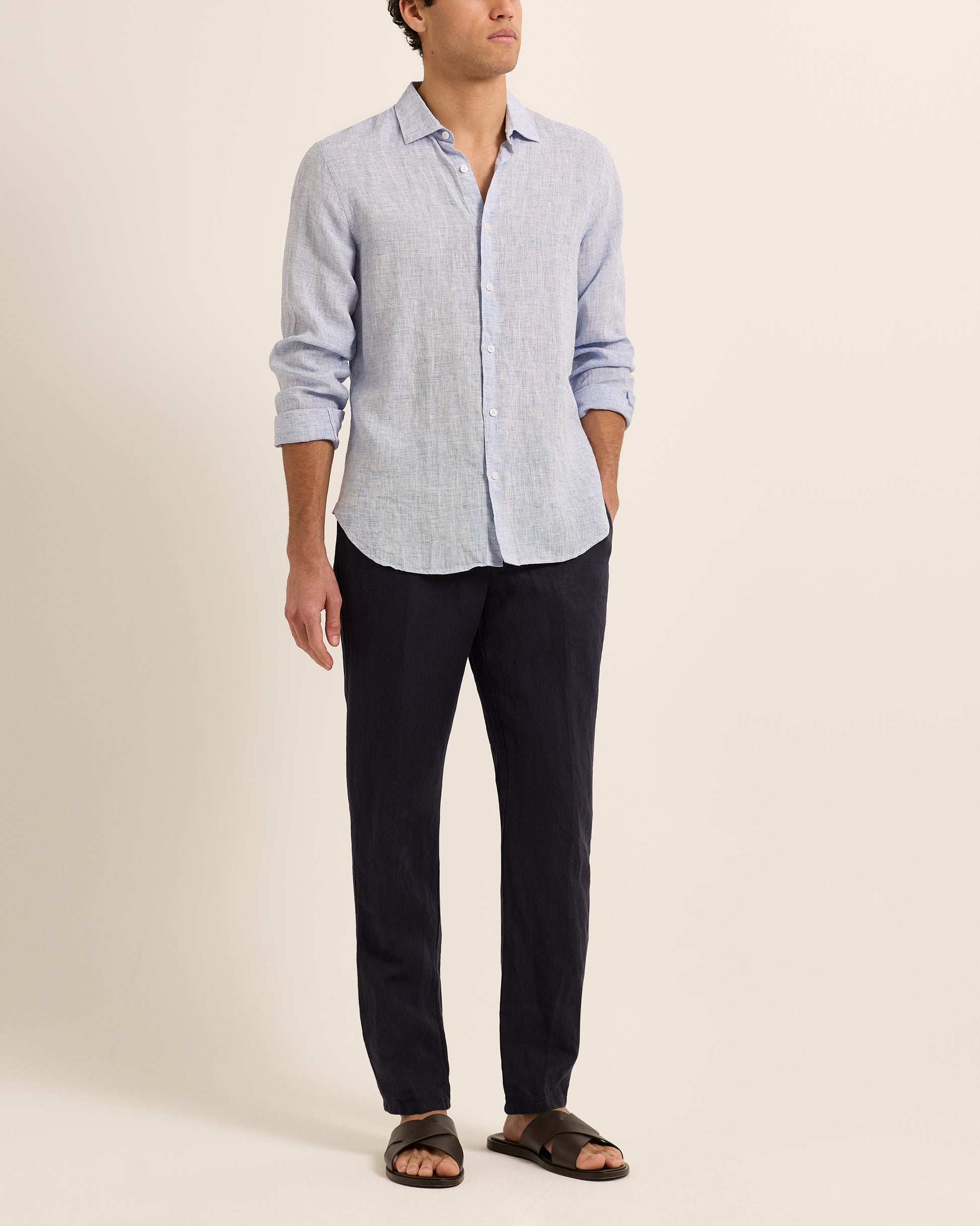 Man wearing light blue linen shirt with dark navy trousers on a white background