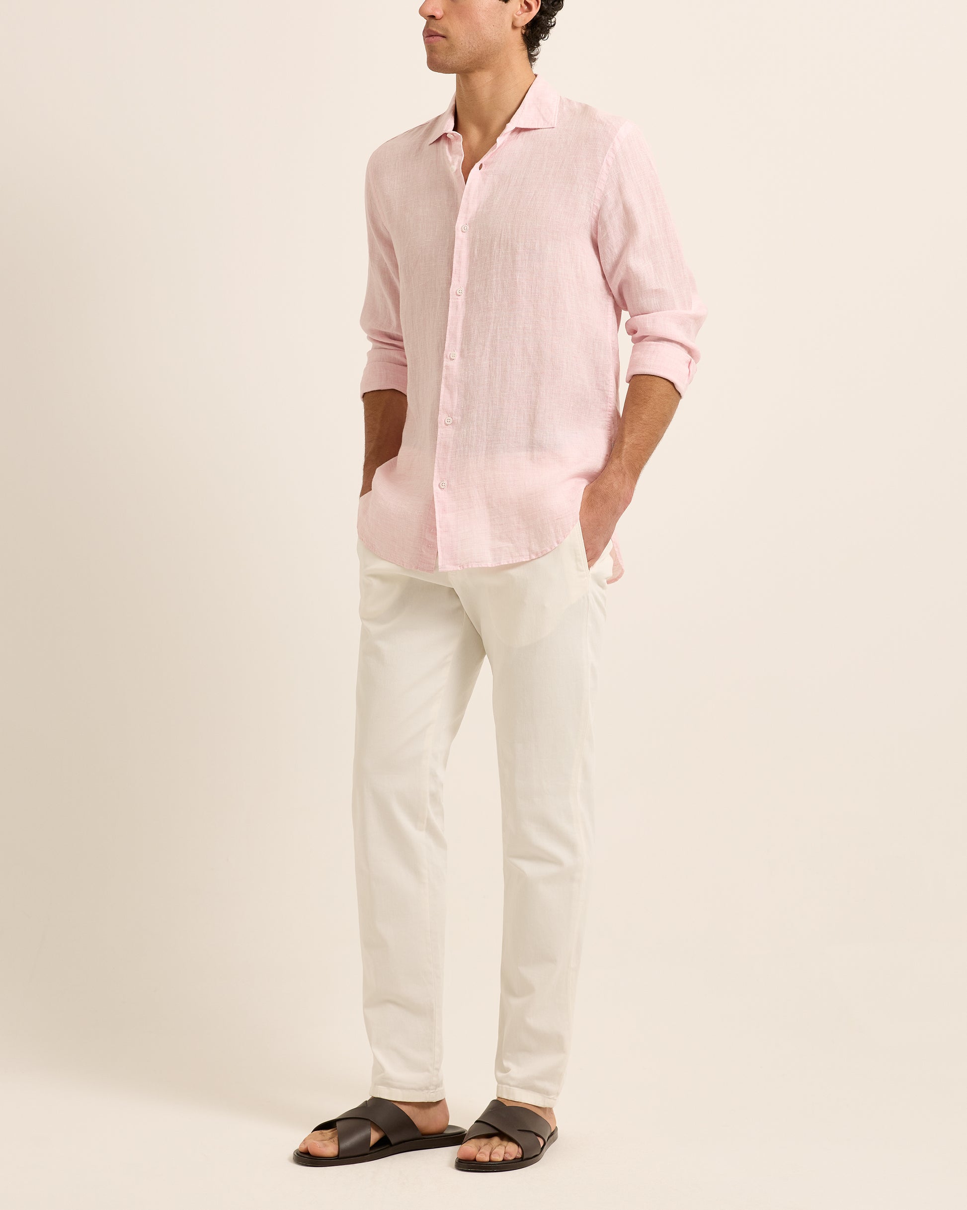 Man wearing light pink linen shirt with white trousers on a white background