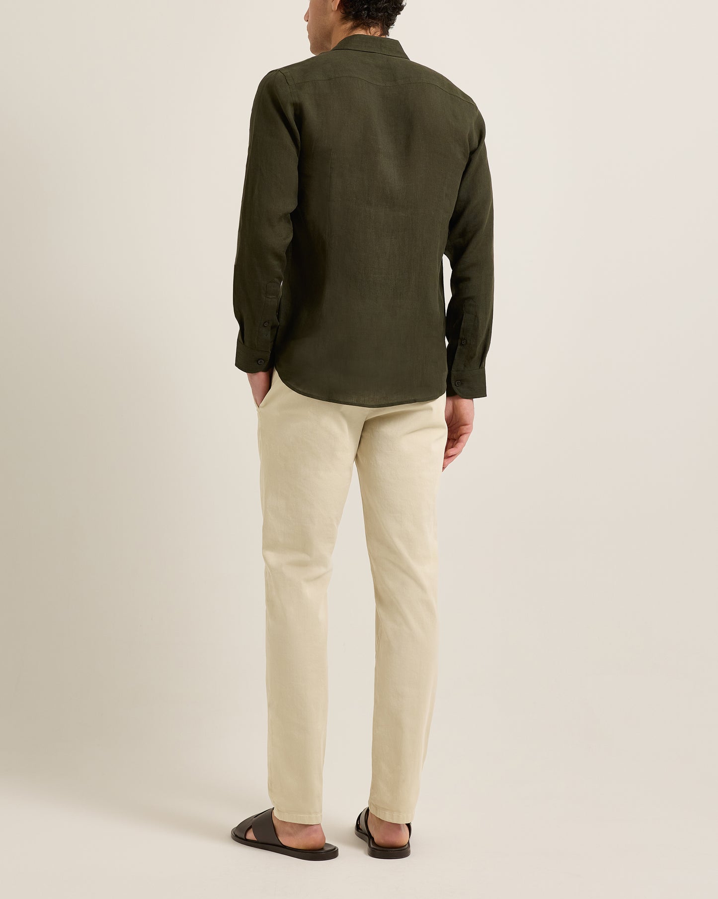 Person wearing a green shirt and beige pants on a plain background