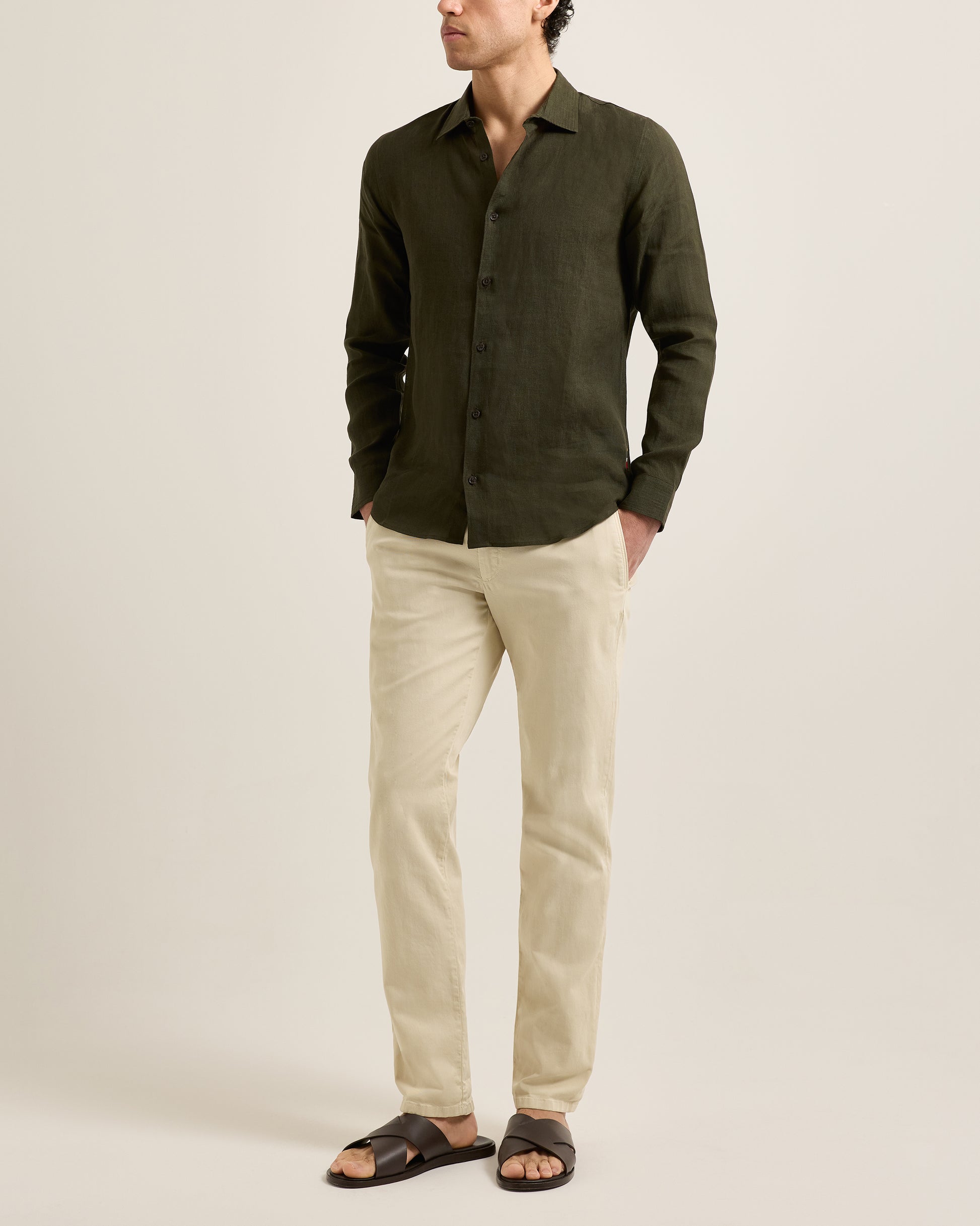 Man wearing a dark green shirt and beige pants on a plain background