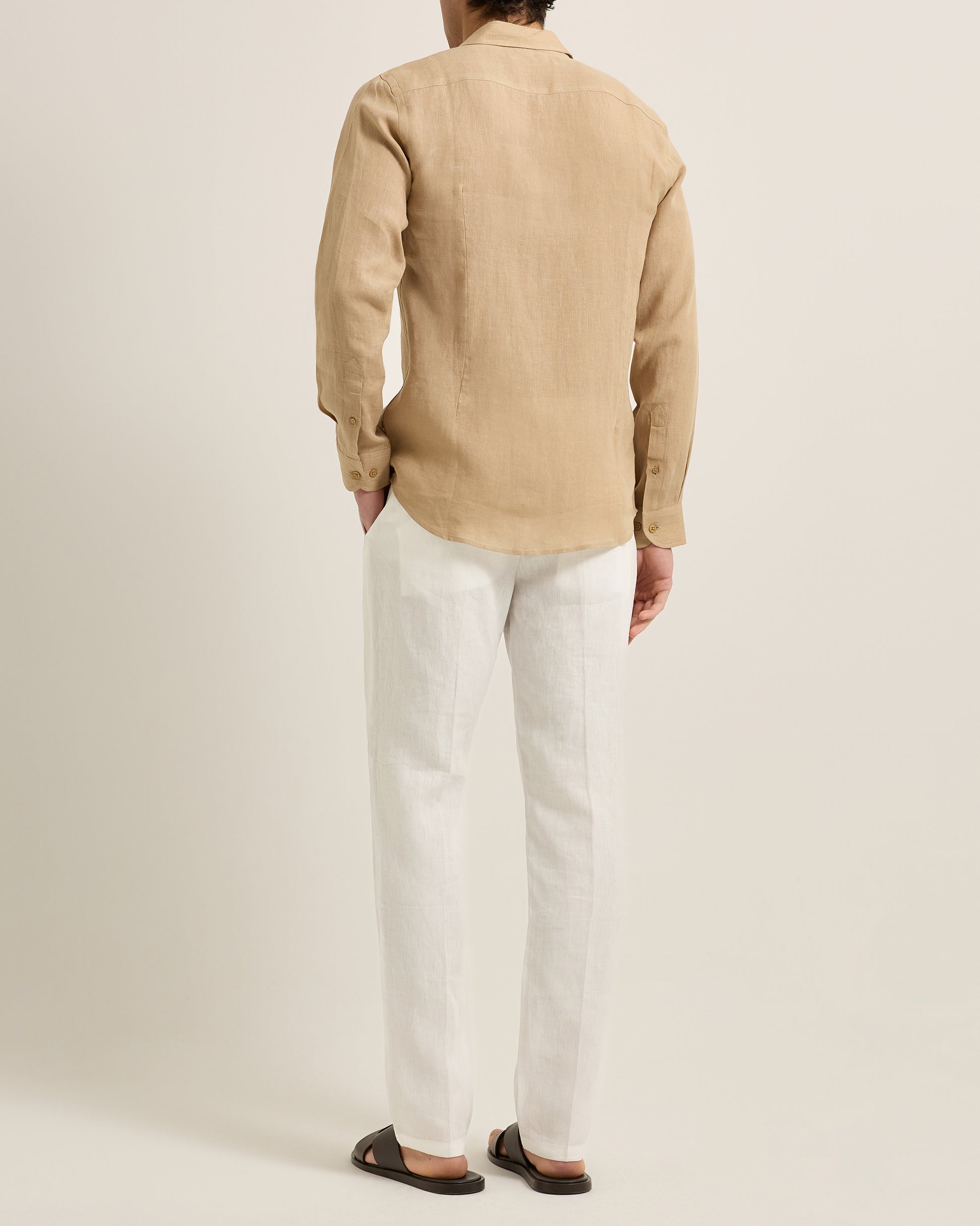 Person wearing a beige shirt and white pants on a plain background