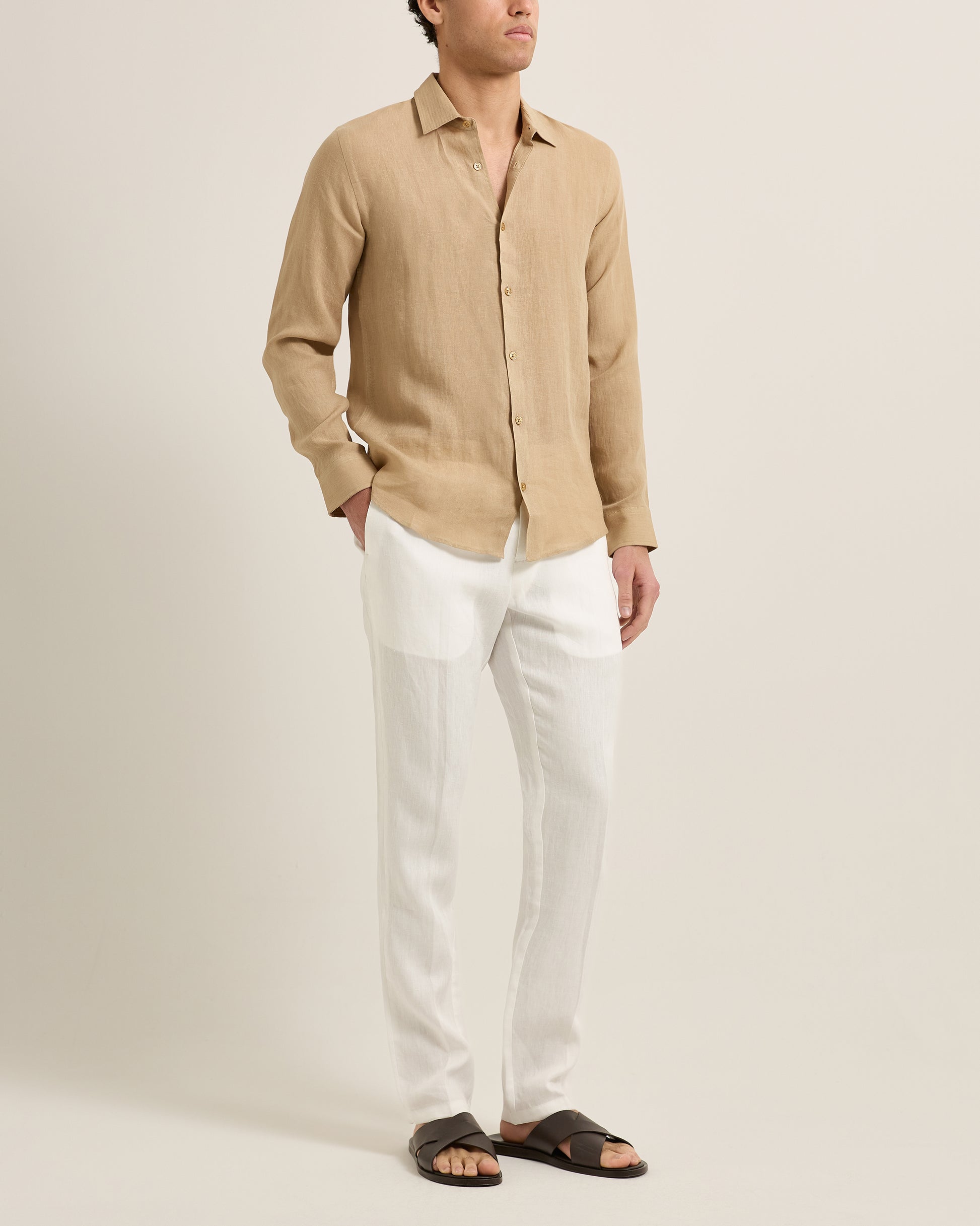 Man wearing a beige linen shirt and white pants on a plain background