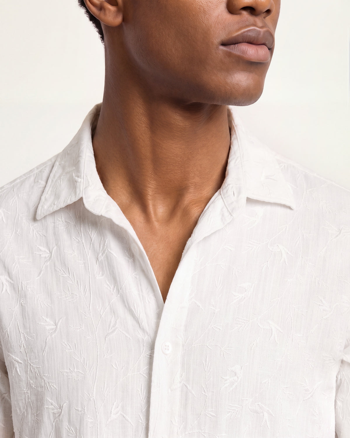 Close-up of a white shirt with featured white embroidery on a plain background