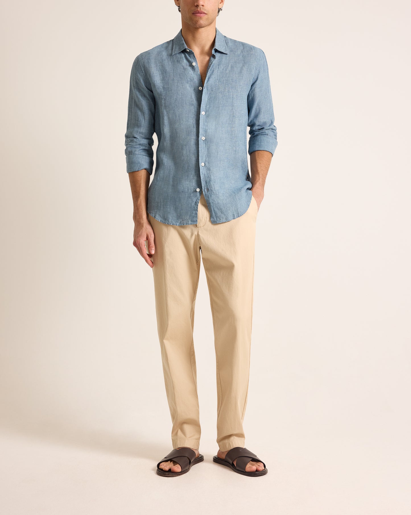 Man wearing a blue shirt and beige pants on a plain background