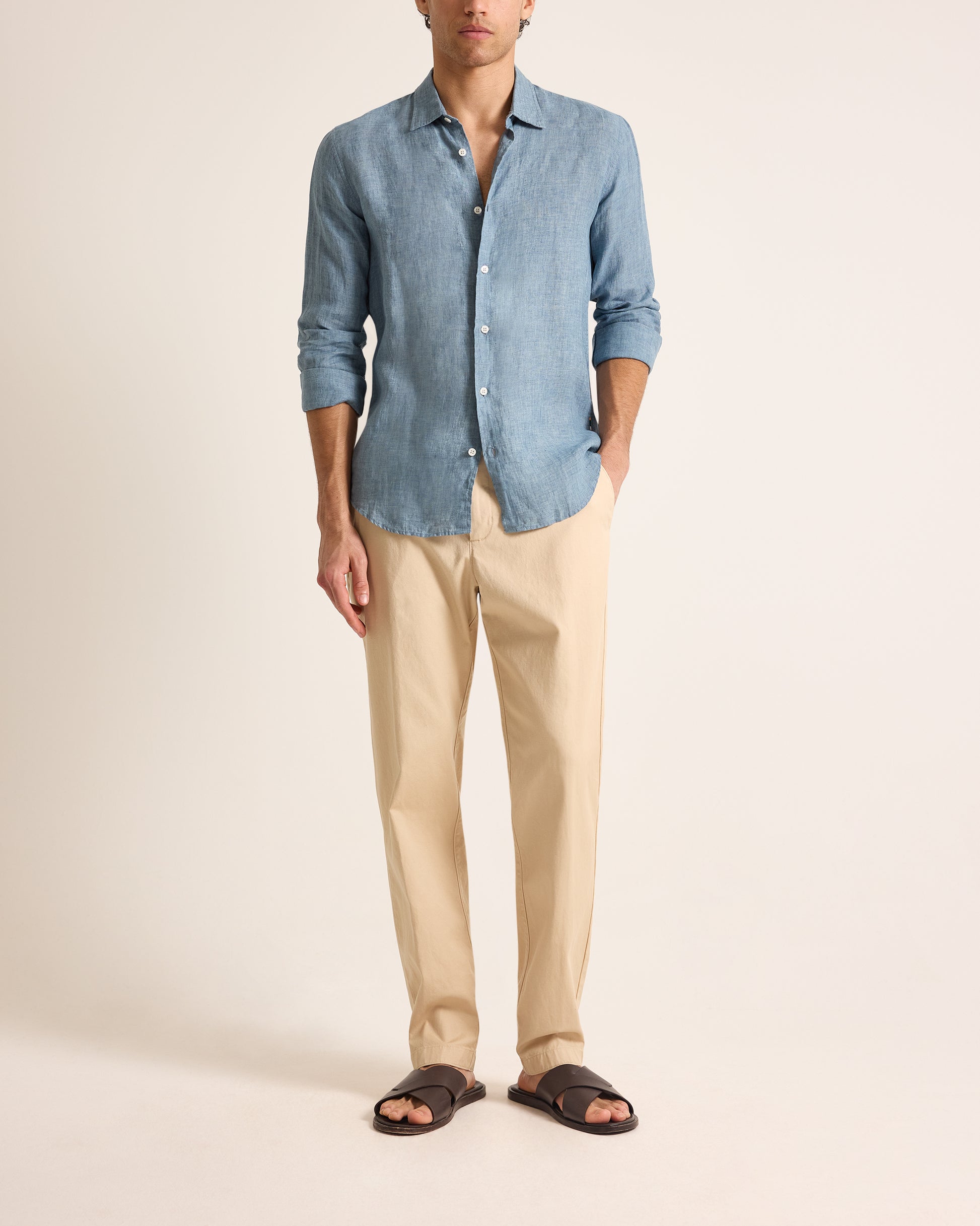 Man wearing a blue shirt and beige pants on a plain background