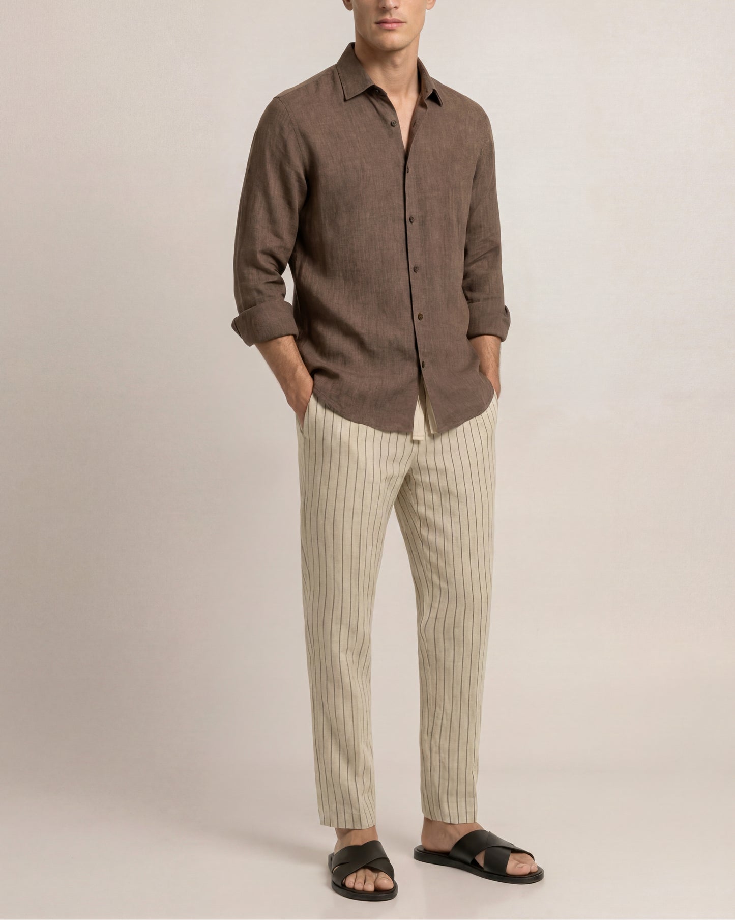 Man wearing a brown shirt and striped pants against a plain background