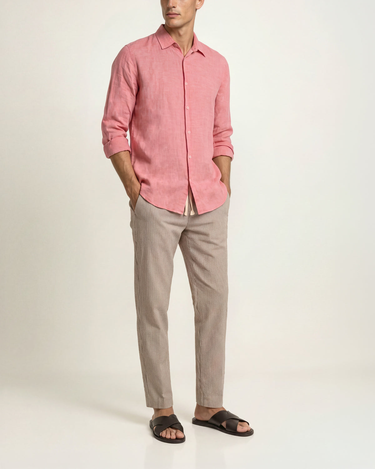 Man wearing a light red long-sleeved shirt paired with white-and-black patterned drawcord-waist trousers and brown sandals on a plain background