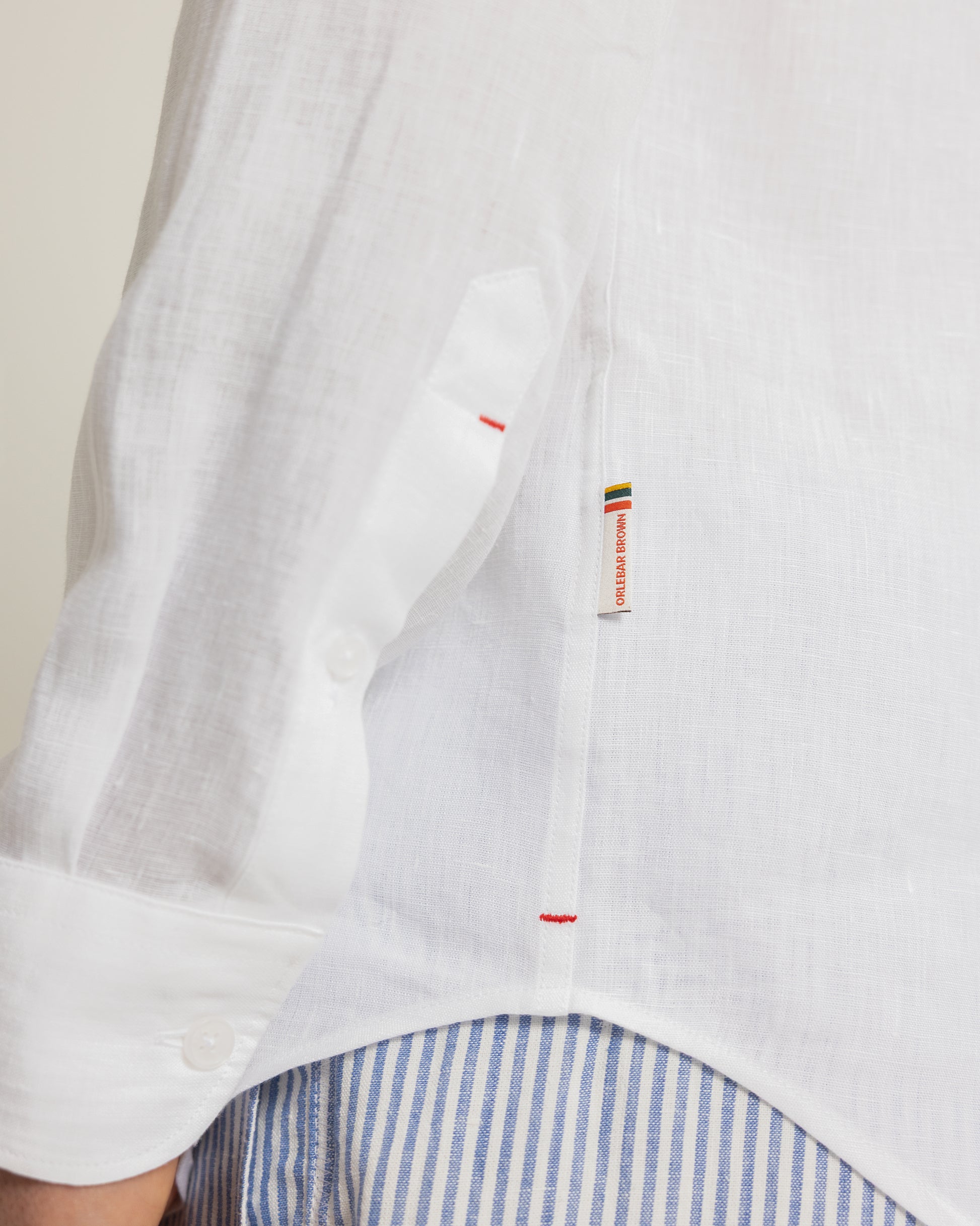 Closeup of white linen shirt with branded tag and worn with blue and white striped trousers