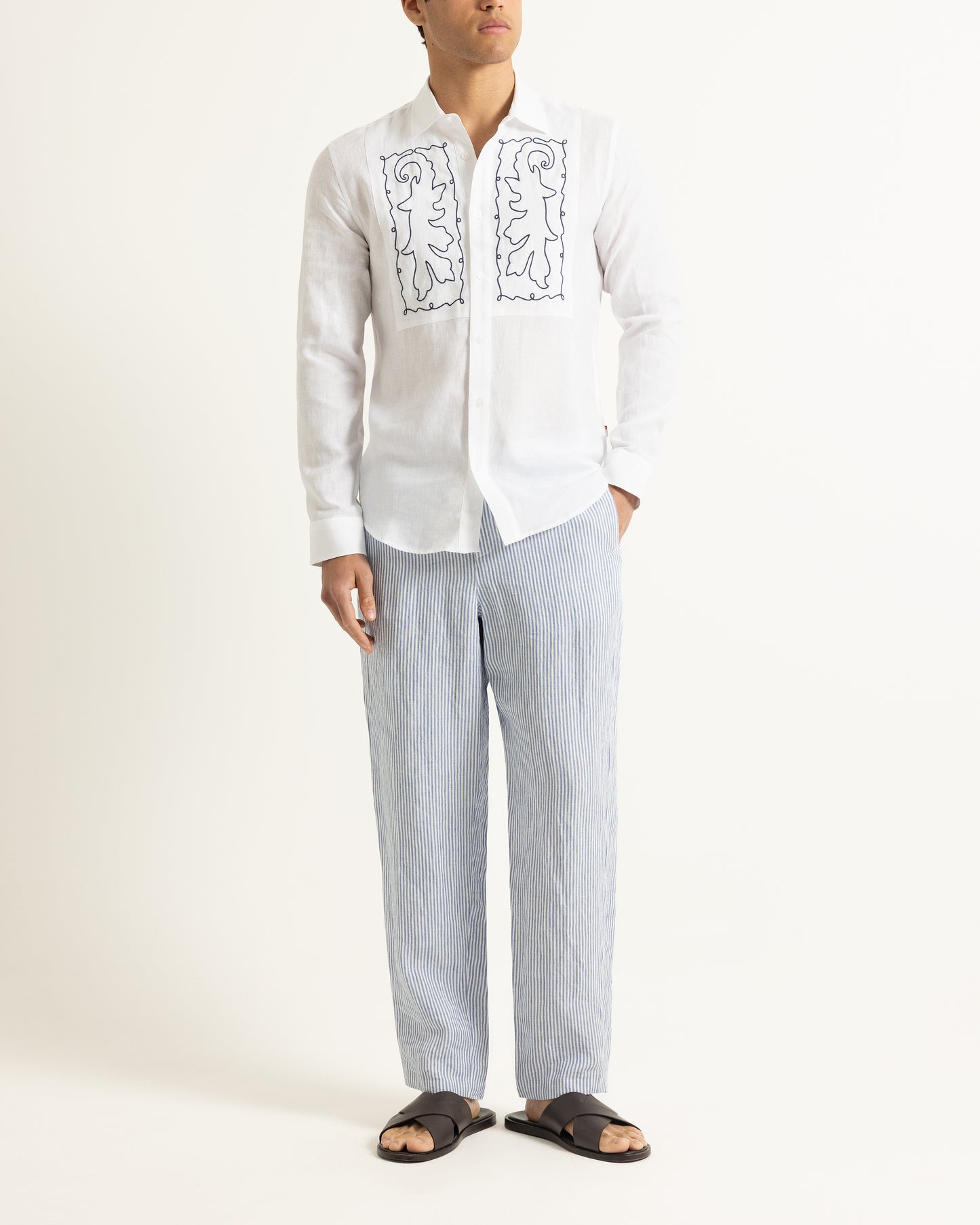 Person wearing a white embroidered shirt and light blue striped pants on a white background