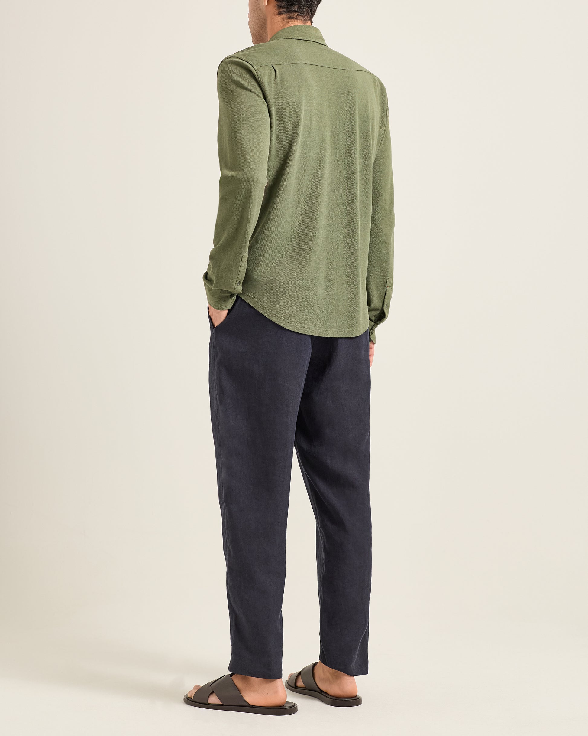 Person wearing a green shirt and dark pants on a beige background