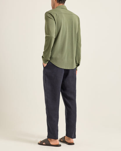 Person wearing a green shirt and dark pants on a beige background