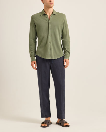 Person wearing a green shirt and dark pants on a beige background