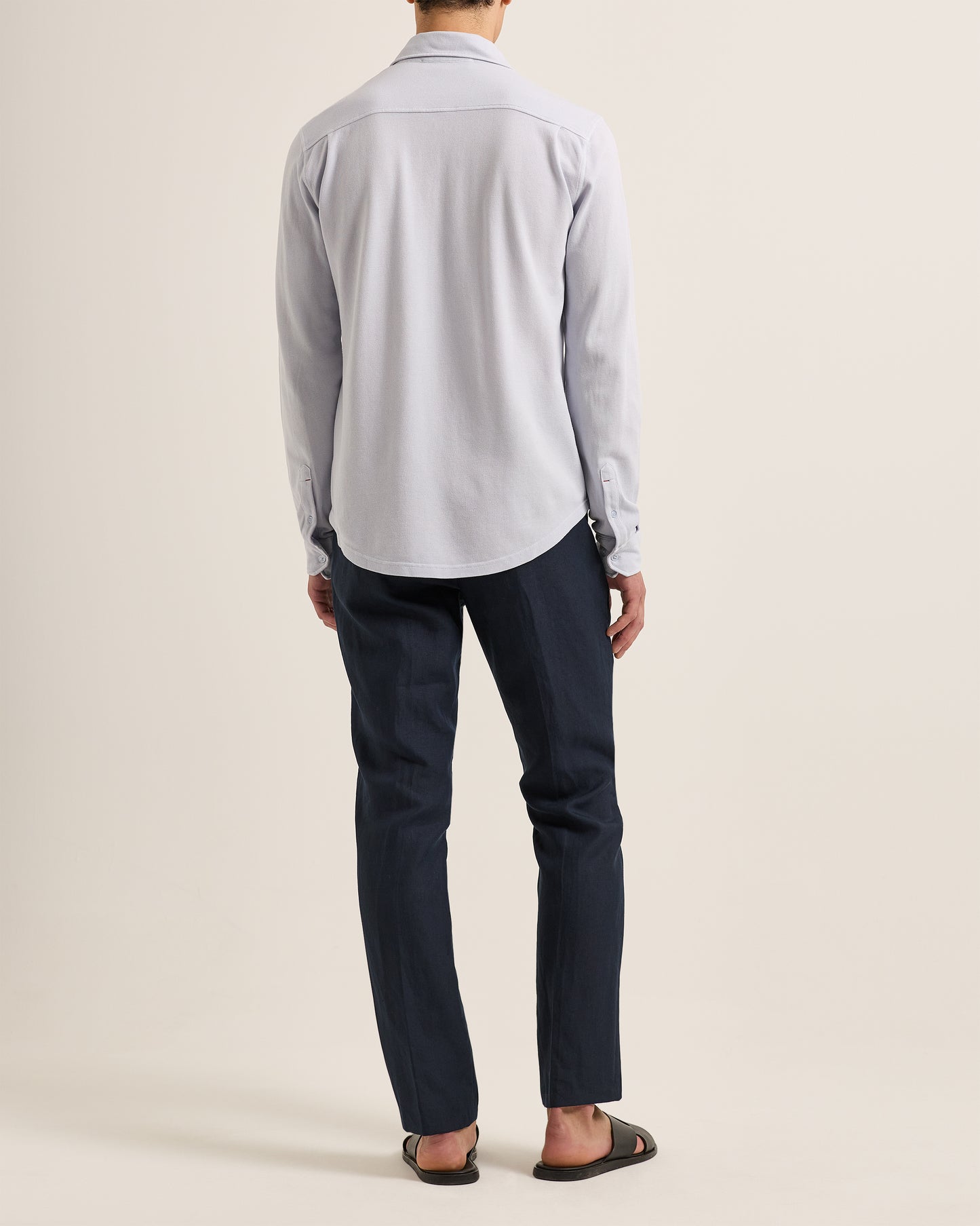 Person wearing a light gray shirt and dark blue pants on a beige background