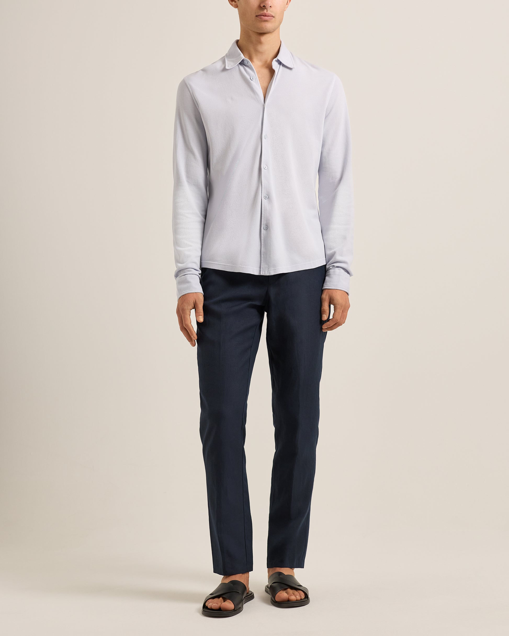 Person wearing a light blue shirt and dark pants on a beige background