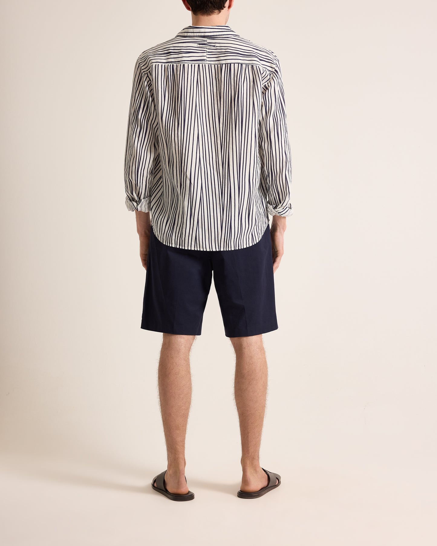 Person wearing a striped shirt and navy shorts on a plain background