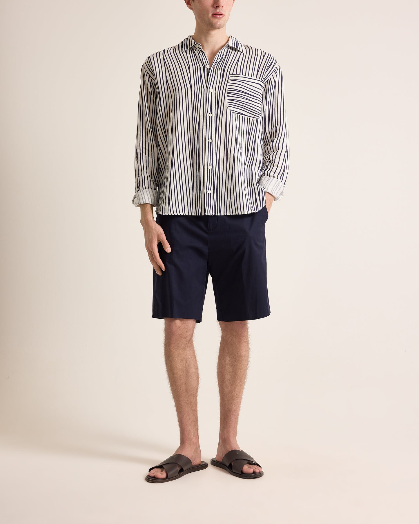 Person wearing a striped shirt and navy shorts on a beige background