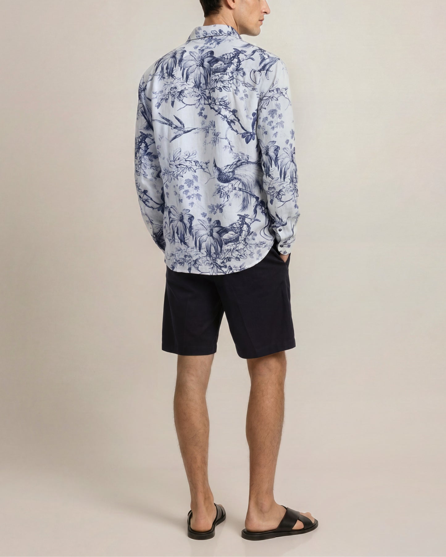 Person wearing a blue patterned shirt and black shorts on a beige background