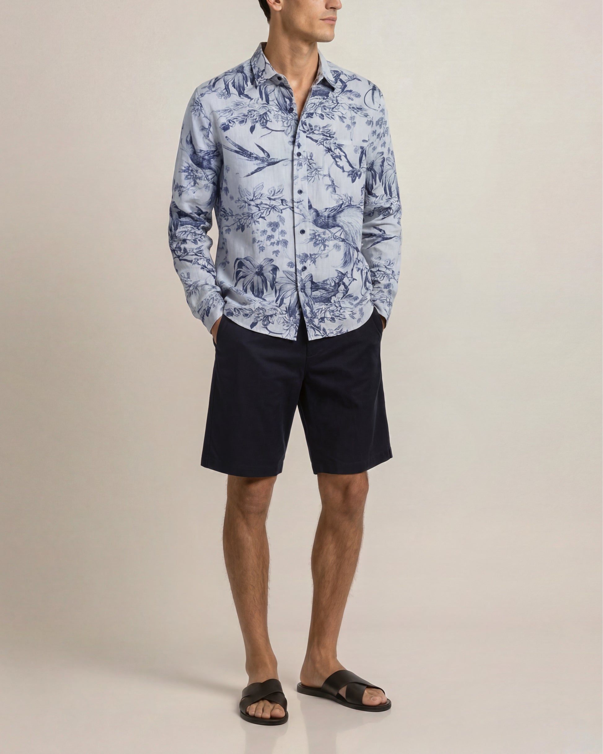 Man wearing a blue patterned shirt and black shorts on a beige background