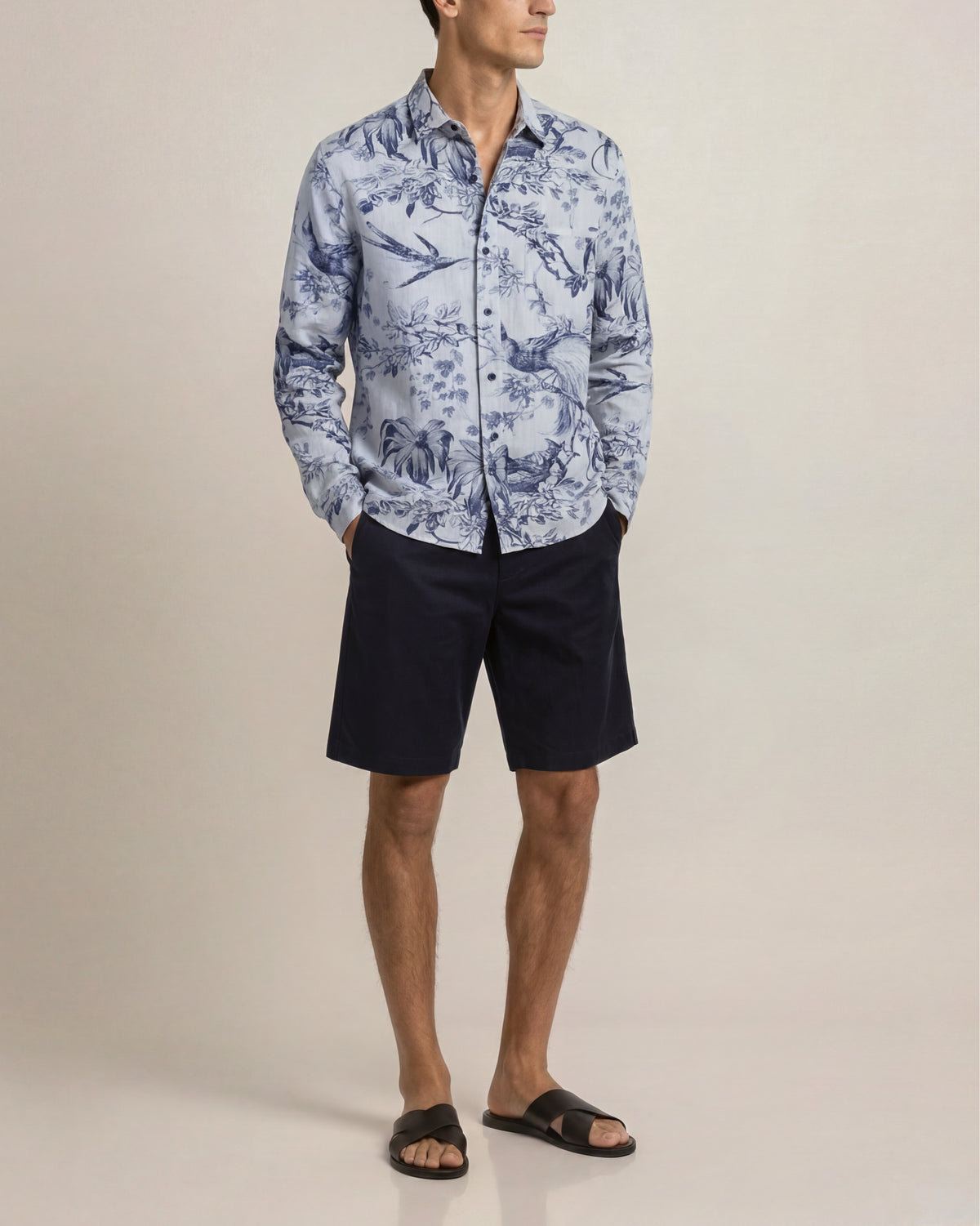 Man wearing a blue patterned shirt and black shorts on a beige background