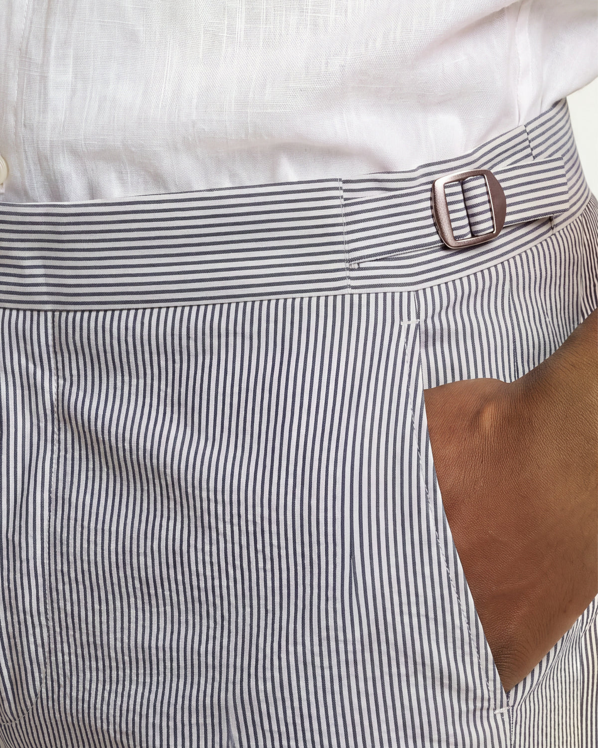 Close-up of a person wearing striped trousers with a side pocket and a silver-toned belt buckle, paired with a white shirt.