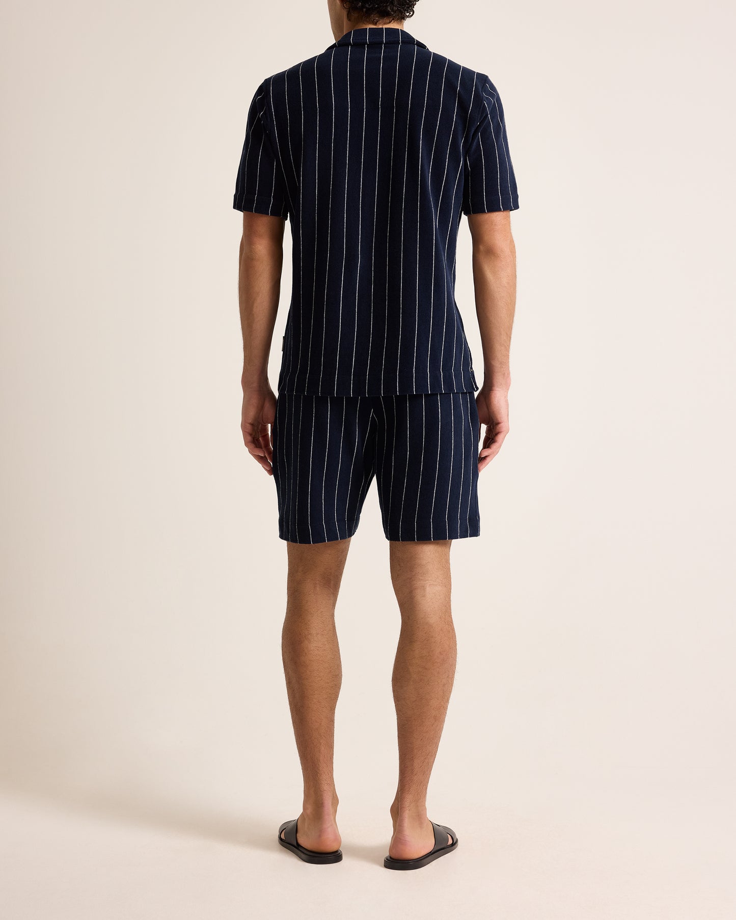 Person wearing a navy pinstripe shirt and shorts set on a beige background
